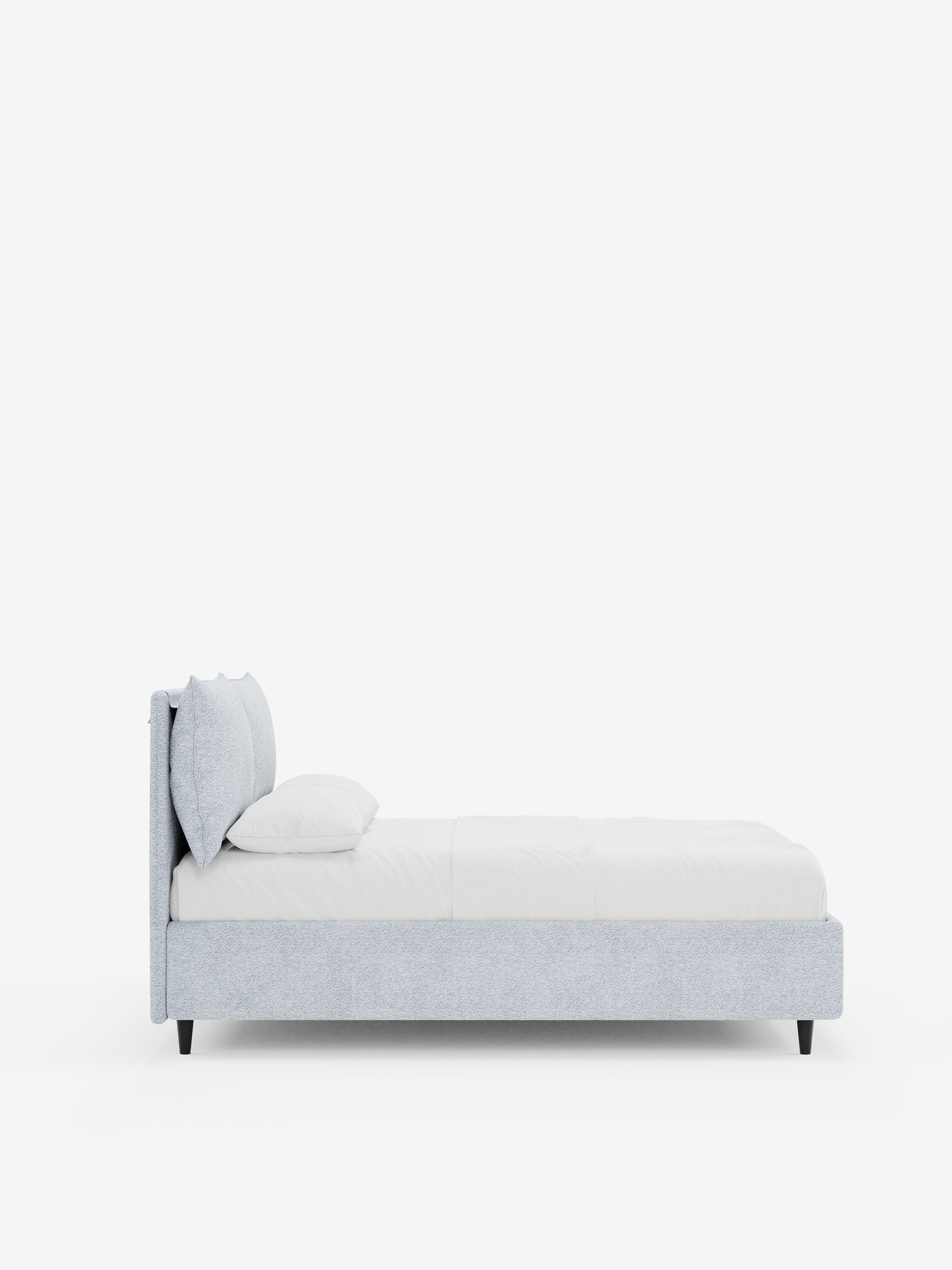 Vista laterale del letto imbottito ZAYRON con contenitore e morbidi cuscini regolabili di Letti.store, caratterizzato da una struttura in tessuto moderno grigio chiaro certificato Oeko-Tex®, una testiera imbottita regolabile, biancheria da letto bianca con due cuscini sovrapposti e gambe angolate nere, il tutto su uno sfondo bianco a tinta unita.