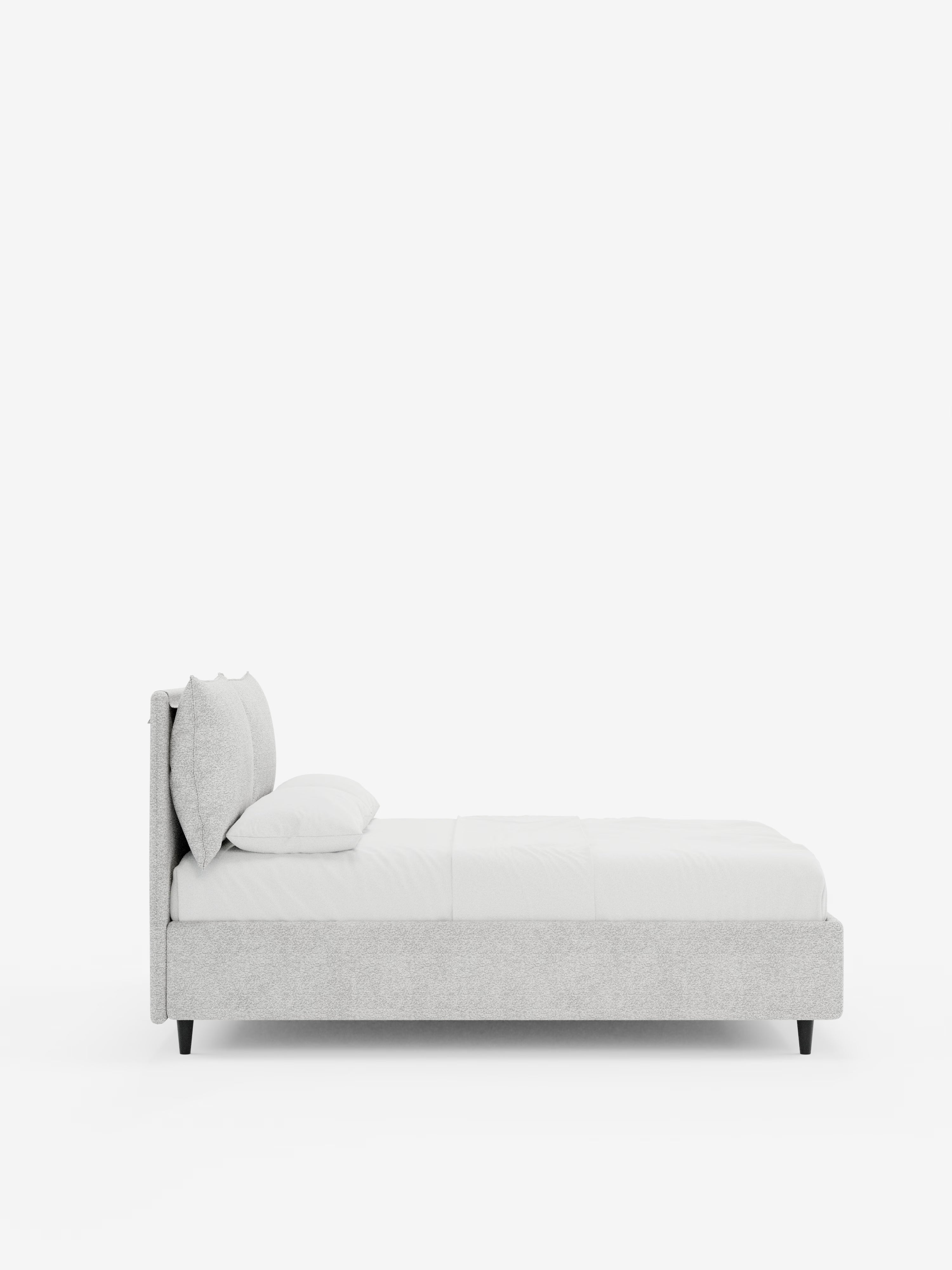 Una vista laterale del letto imbottito ZAYRON con contenitore e morbidi cuscini regolabili di Letti.store ne mette in risalto il design moderno e minimalista, realizzato in tessuto grigio chiaro certificato Oeko-Tex®, caratterizzato da una testiera imbottita, biancheria da letto bianca con un unico cuscino e sostenuto da quattro gambe corte nere su uno sfondo bianco a tinta unita.