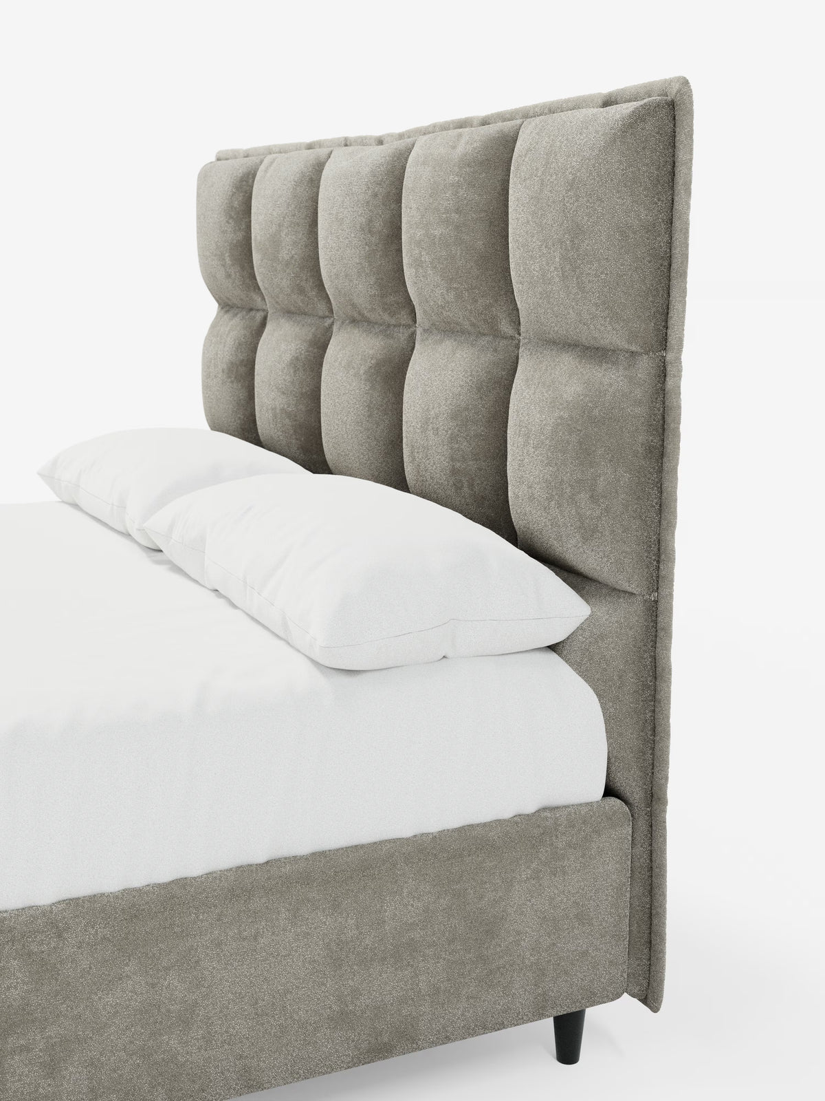 Un primo piano del letto imbottito con contenitore AURO di Letti.store, caratterizzato da una testiera alta e capitonné, rivestita in tessuto ciniglia grigio certificato Oeko-Tex® con ampi pannelli quadrati. Il letto è abbellito da un lenzuolo con angoli bianco e due cuscini bianchi, mentre la struttura imbottita è in tinta con il tessuto della testiera e poggia su corte gambe nere.