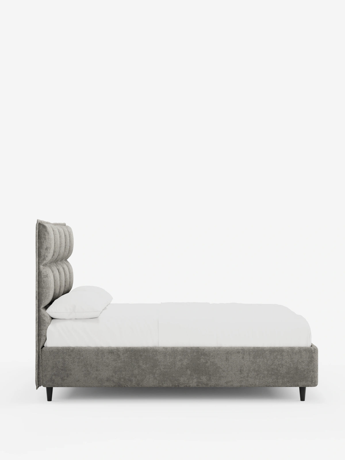 Vista laterale di un letto imbottito AURO con contenitore e testiera alta capitonné in ciniglia Oeko-Tex® di colore grigio, caratterizzata da una testiera alta capitonné, biancheria da letto di un bianco brillante e piccole gambe nere su uno sfondo chiaro e uniforme.