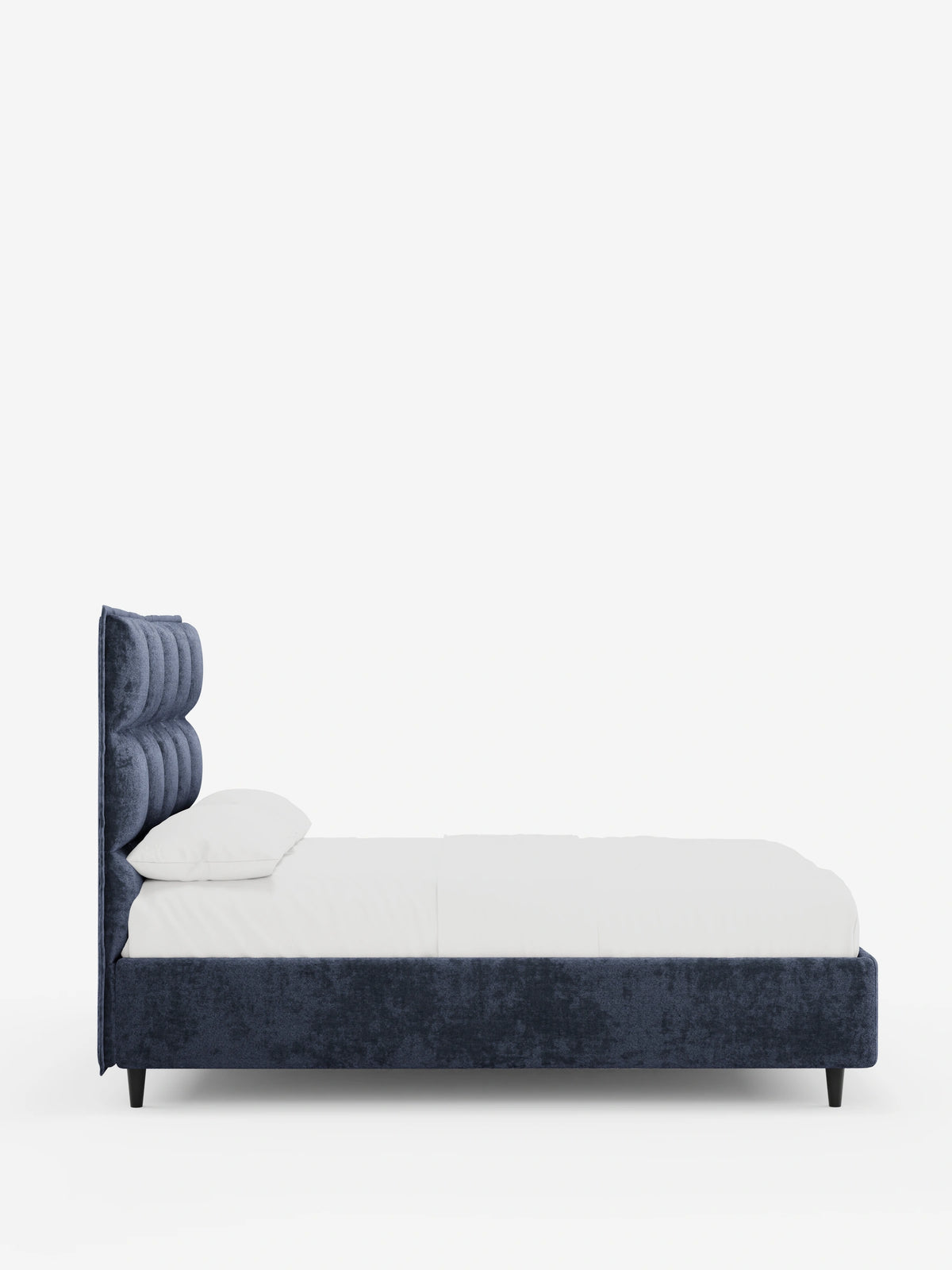Profilo laterale di un letto imbottito AURO blu scuro con finitura testurizzata, dotato di vano contenitore e testiera alta capitonné in ciniglia Oeko-Tex®, con gambe corte nere, rivestito con semplice biancheria da letto bianca su uno sfondo bianco a tinta unita.