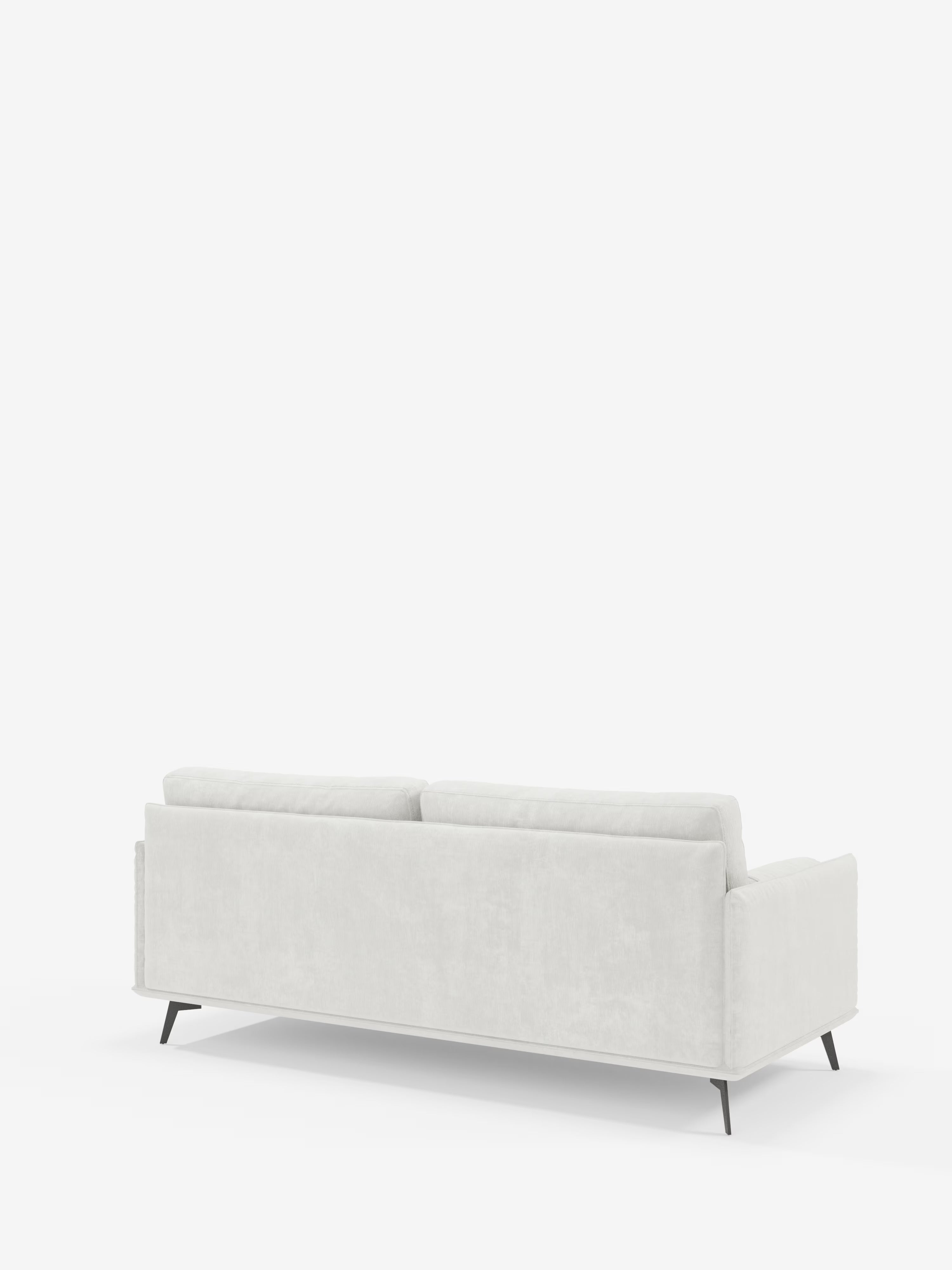 Il divano lineare a 2 posti “Basalto” di Divani.Store, in grigio chiaro e dallo stile contemporaneo, è ripreso di profilo dal retro. Caratterizzato da un profilo basso, due spaziosi cuscini dello schienale, linee pulite e una base sottile in metallo nero, questo divano minimalista è rivestito in tessuto smacchiabile T31. Il suo design raffinato e funzionale risalta sullo sfondo bianco.