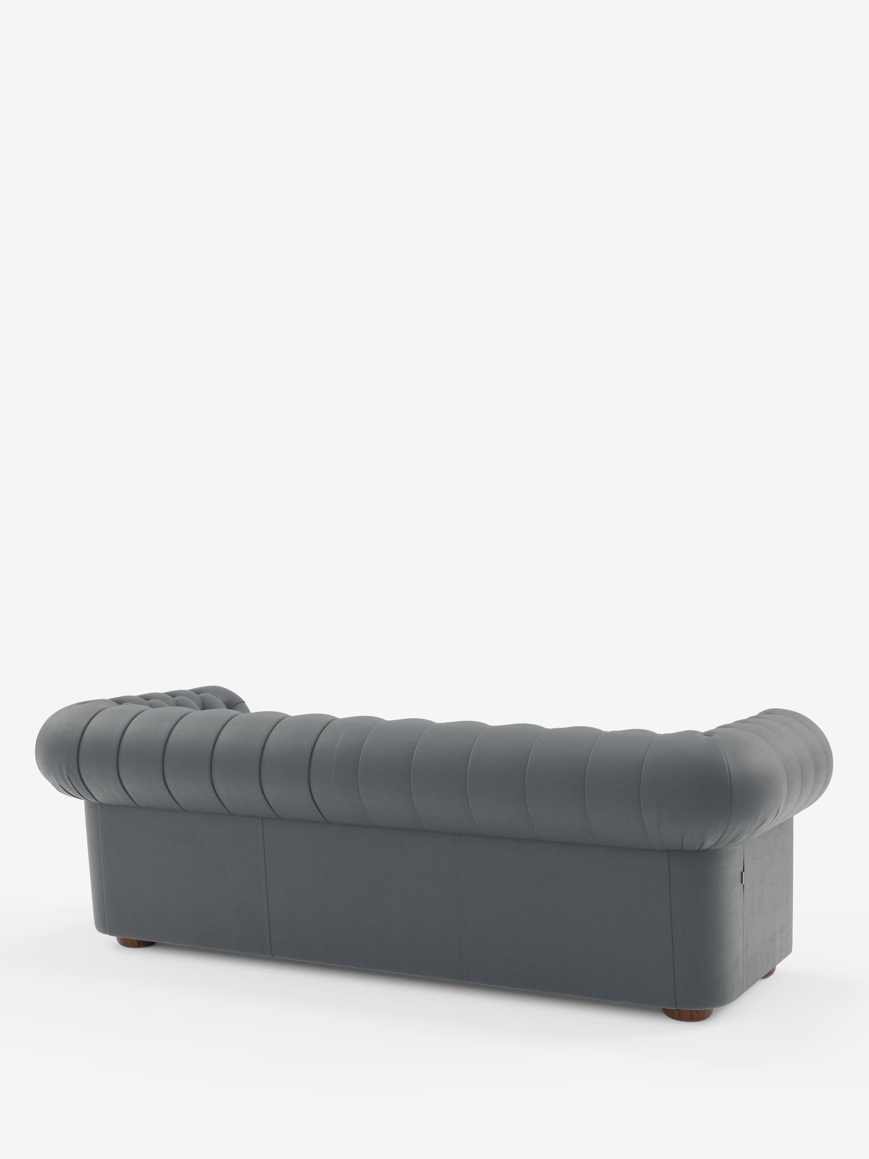 Un divano Chester 4 Posti 3 sedute in vera pelle, colore grigio scuro – Chesterfield Capitonné Artigianale di Divani.Store – è ripreso da dietro in un’angolazione che ne mette in risalto i braccioli arrotondati e lo schienale con l’elegante trapuntatura. Realizzato con maestria in vera pelle, questo divano artigianale poggia su piccole gambe rotonde in legno e si staglia su uno sfondo bianco a tinta unita.