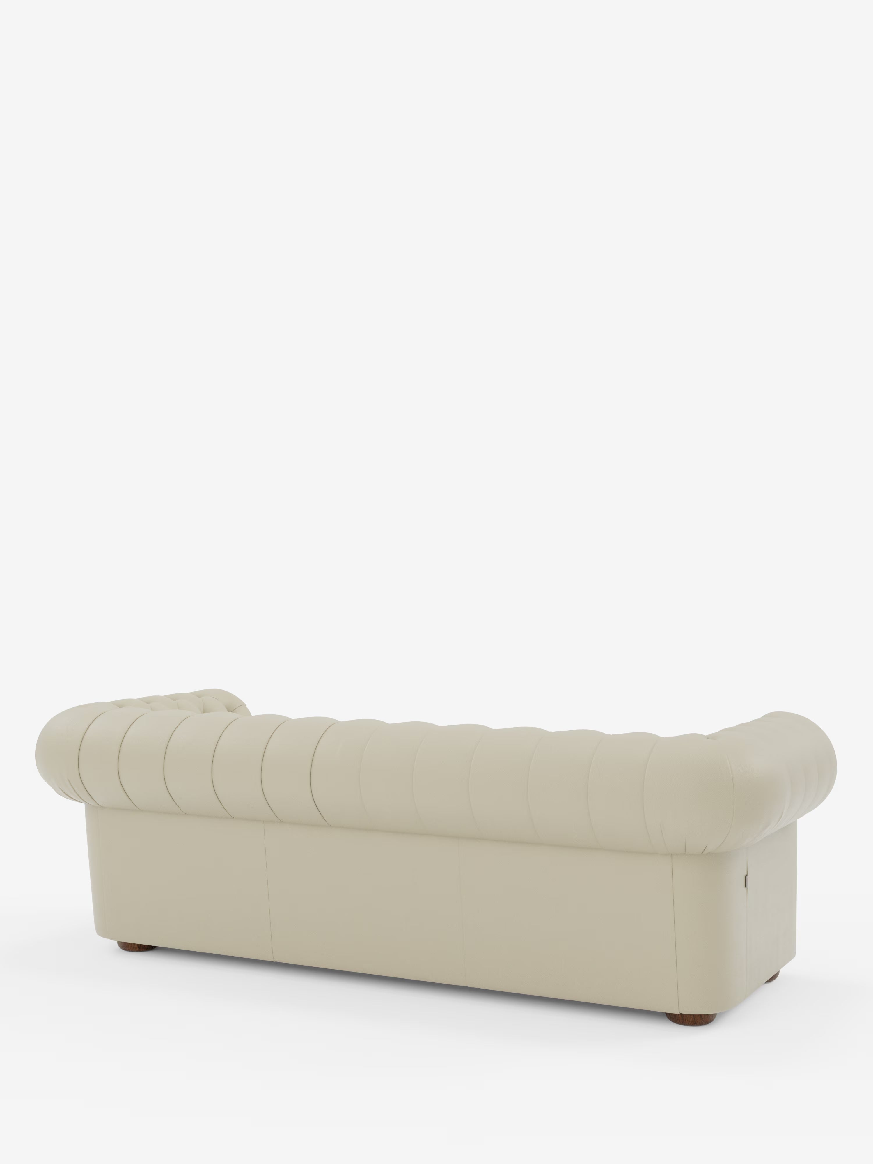 Un divano in pelle capitonné color crema — il modello Chester 4 Posti 3 sedute in Vera Pelle – Chesterfield Capitonné Artigianale di Divani.Store — è ripreso da dietro con una leggera angolazione, mettendo in risalto i braccioli e lo schienale arrotondati. Appoggiato su piccoli piedini rotondi in legno e incorniciato da uno sfondo bianco a tinta unita, questo divano Chesterfield artigianale mette in mostra una squisita maestria in ogni suo elegante dettaglio.