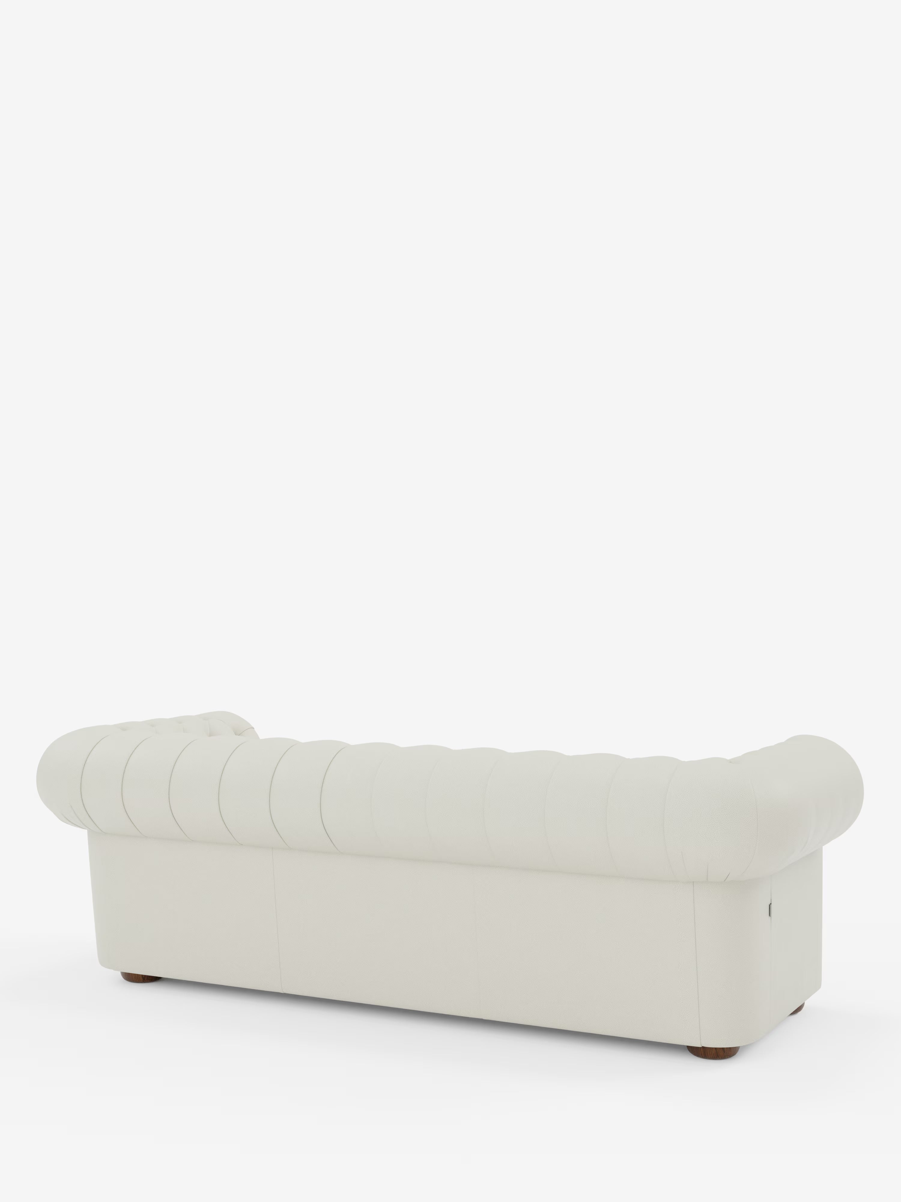 Una vista posteriore del divano Divani.Store Chester 4 Posti 3 sedute in Vera Pelle – Chesterfield Capitonné Artigianale mette in risalto i braccioli elegantemente ricurvi e lo schienale rivestito in vera pelle lavorata a mano, con gambe corte in legno, il tutto su uno sfondo bianco a tinta unita.