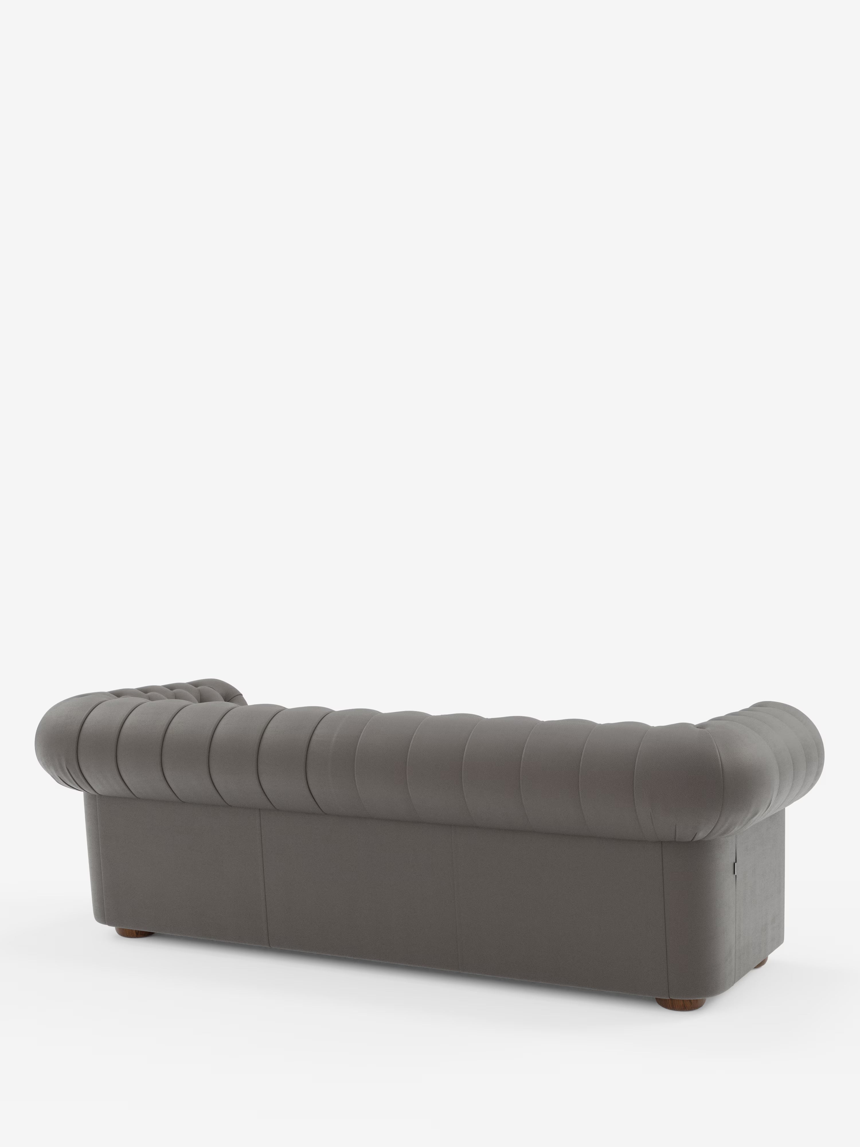 Un divano Chester 4 Posti 3 sedute in vera pelle, colore grigio scuro – Chesterfield Capitonné Artigianale di Divani.Store – è ripreso dal retro su uno sfondo bianco. Realizzato in Italia, questo divano mette in risalto la sua lussuosa parte posteriore imbottita, caratterizzata da una profonda trapuntatura a bottoni e da braccioli e schienale arrotondati alla stessa altezza. Il divano è sostenuto da quattro gambe corte e rotonde in legno, che conferiscono al mobile un tocco classico.