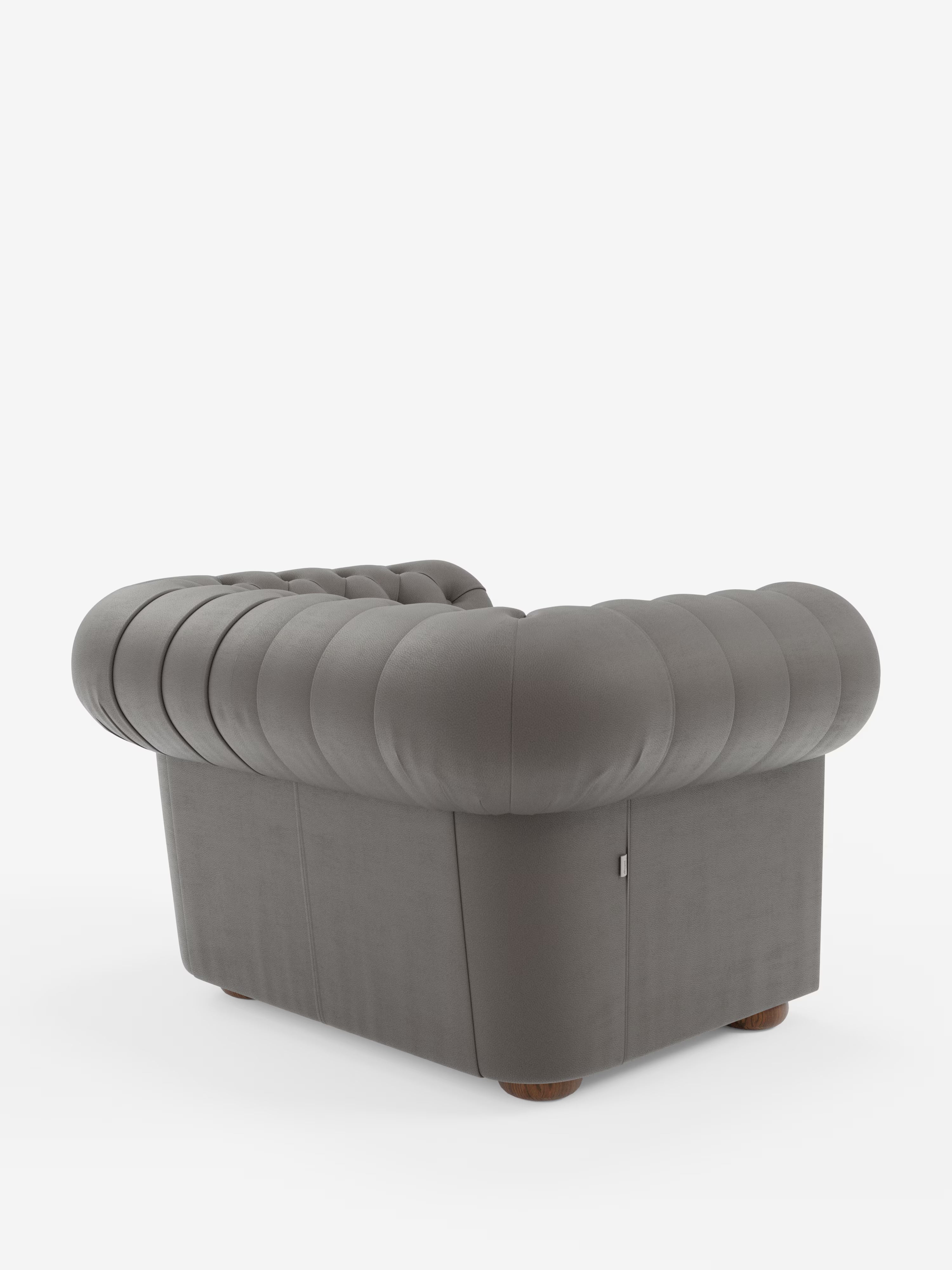 Una lussuosa poltrona Chester in vera pelle spessorata con capitonné artigianale di Divani.Store, caratterizzata da una raffinata trapuntatura artigianale a bottoni, schienale e braccioli bassi, piedini in legno e una silhouette squadrata e moderna. Ripresa da dietro in prospettiva su uno sfondo bianco, questa poltrona in pelle grigia — con i suoi bordi arrotondati e le profonde pieghe orizzontali — coniuga l’eleganza senza tempo del design classico con il fascino contemporaneo.