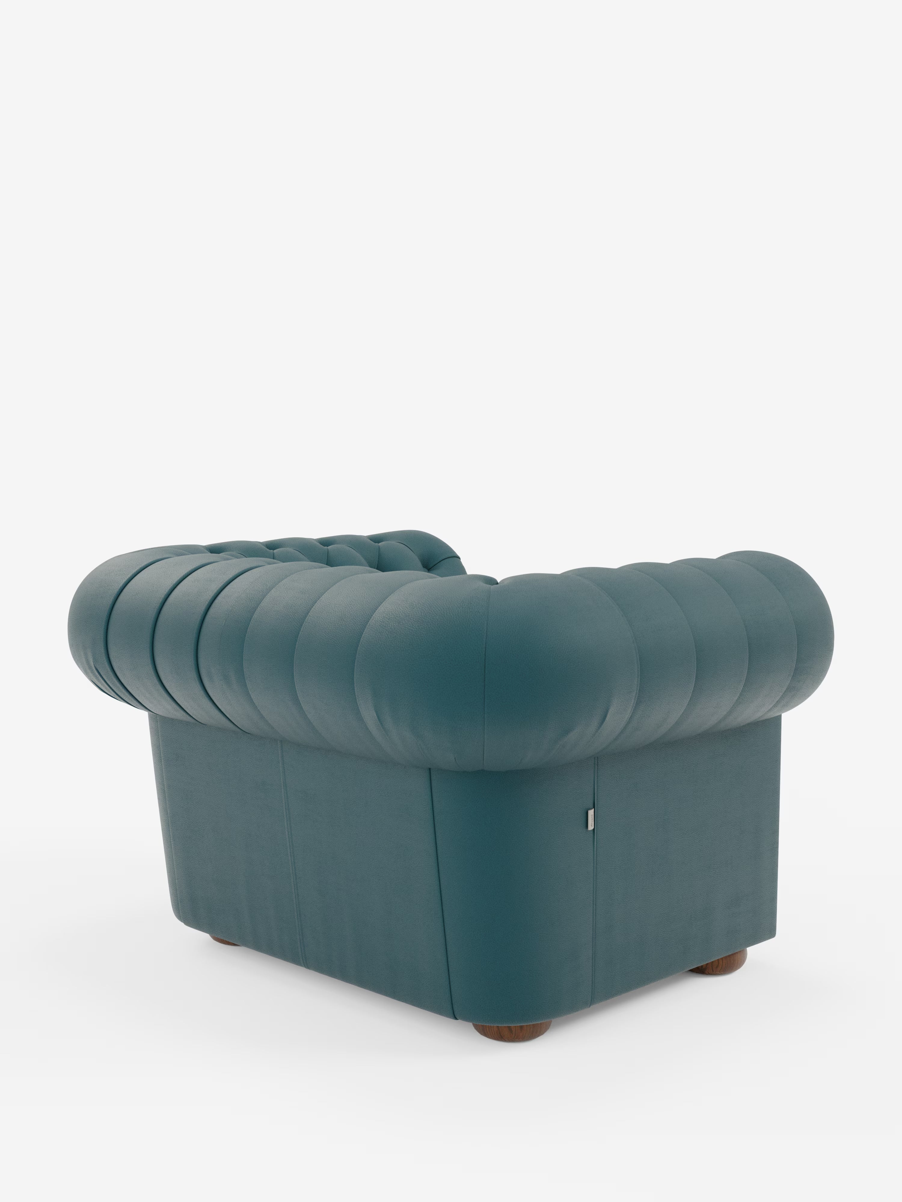 La poltrona Chester di Divani.Store, realizzata in vera pelle spessorata con capitonné artigianale, è una poltrona color verde acqua con rivestimento capitonné, caratterizzata da schienale e braccioli arrotondati e imbottiti. Appoggiata su brevi gambe in legno, la poltrona è raffigurata in una prospettiva posteriore sinistra su uno sfondo bianco a tinta unita. Il rivestimento liscio e le cuciture profonde le conferiscono un aspetto lussuoso e accogliente.
