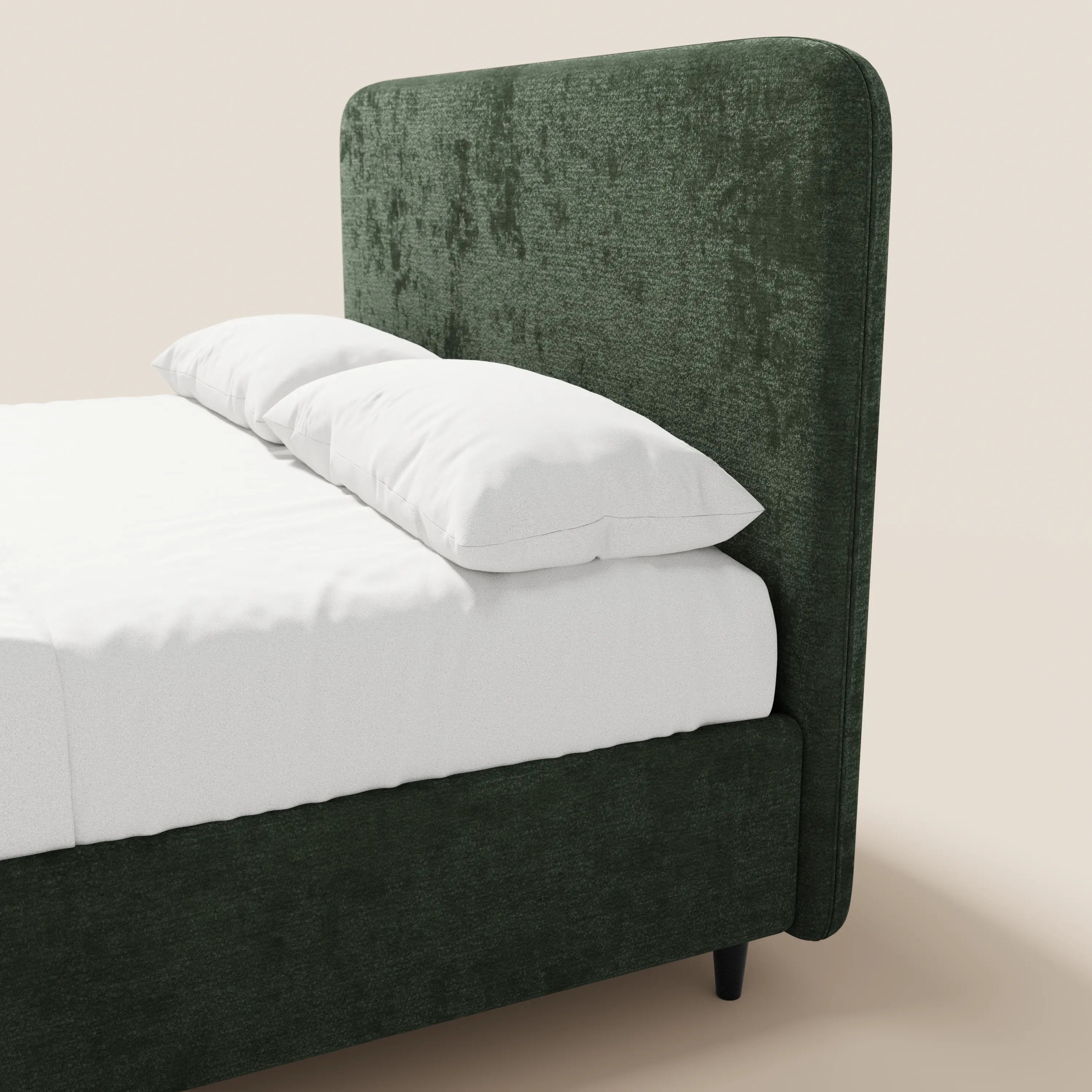 Una vista laterale ravvicinata del letto KAELOS minimal imbottito di Letti.store mostra una testiera alta in ciniglia verde scuro e una struttura con gambe alte, lenzuola bianche e due cuscini bianchi sovrapposti su uno sfondo beige chiaro.