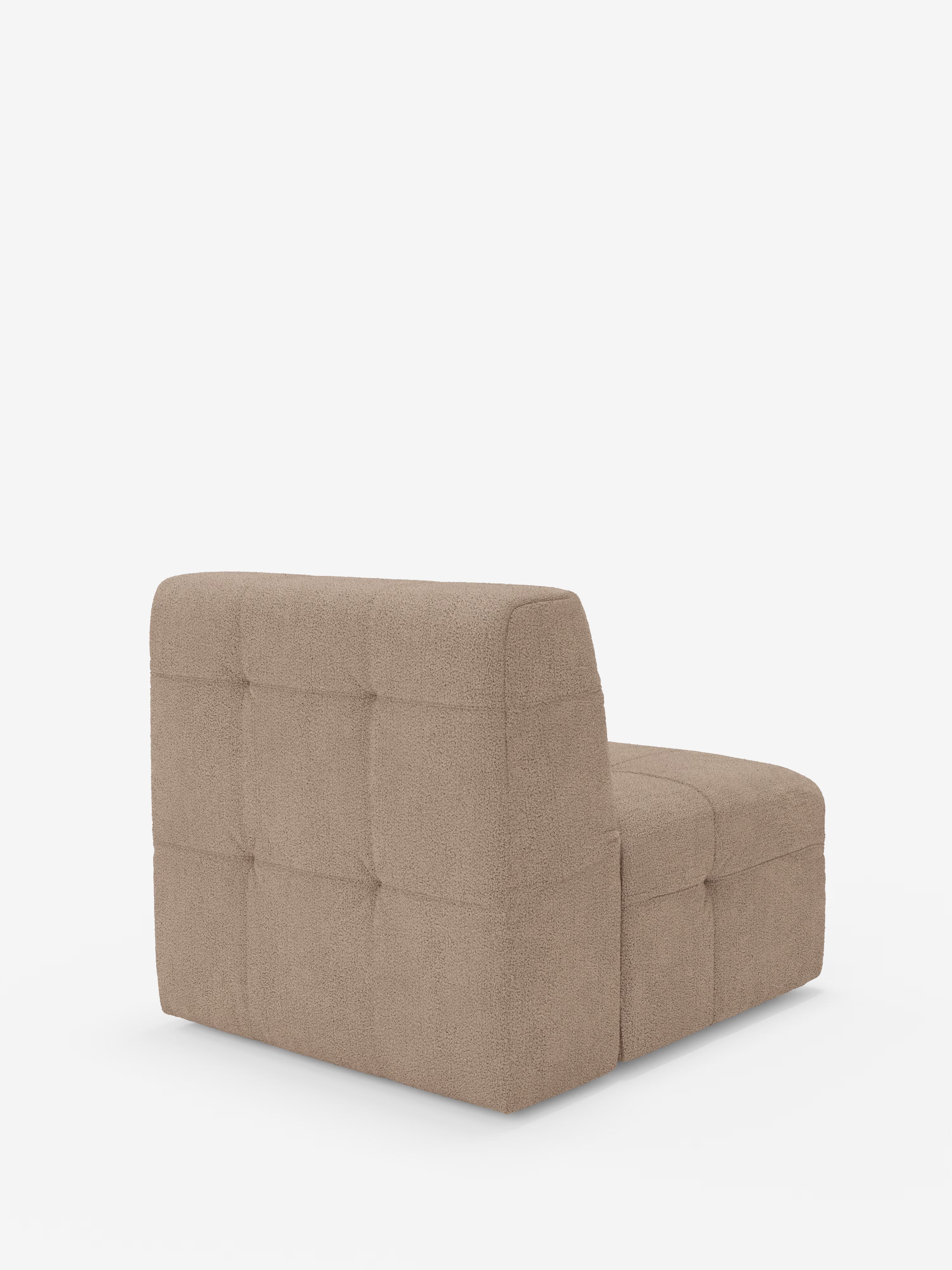Una poltrona modulare senza braccioli, la Mosaic modulo poltrona 77 cm di Divani.Store, è rivestita in tessuto bouclé T21 color taupe resistente alle macchie, con dettagli capitonné (imbottiti) e una silhouette squadrata, raffinata e minimalista, ispirata al design classico delle poltrone. Immagine ripresa da una prospettiva obliqua da sinistra, con lo schienale in primo piano su uno sfondo bianco a tinta unita.