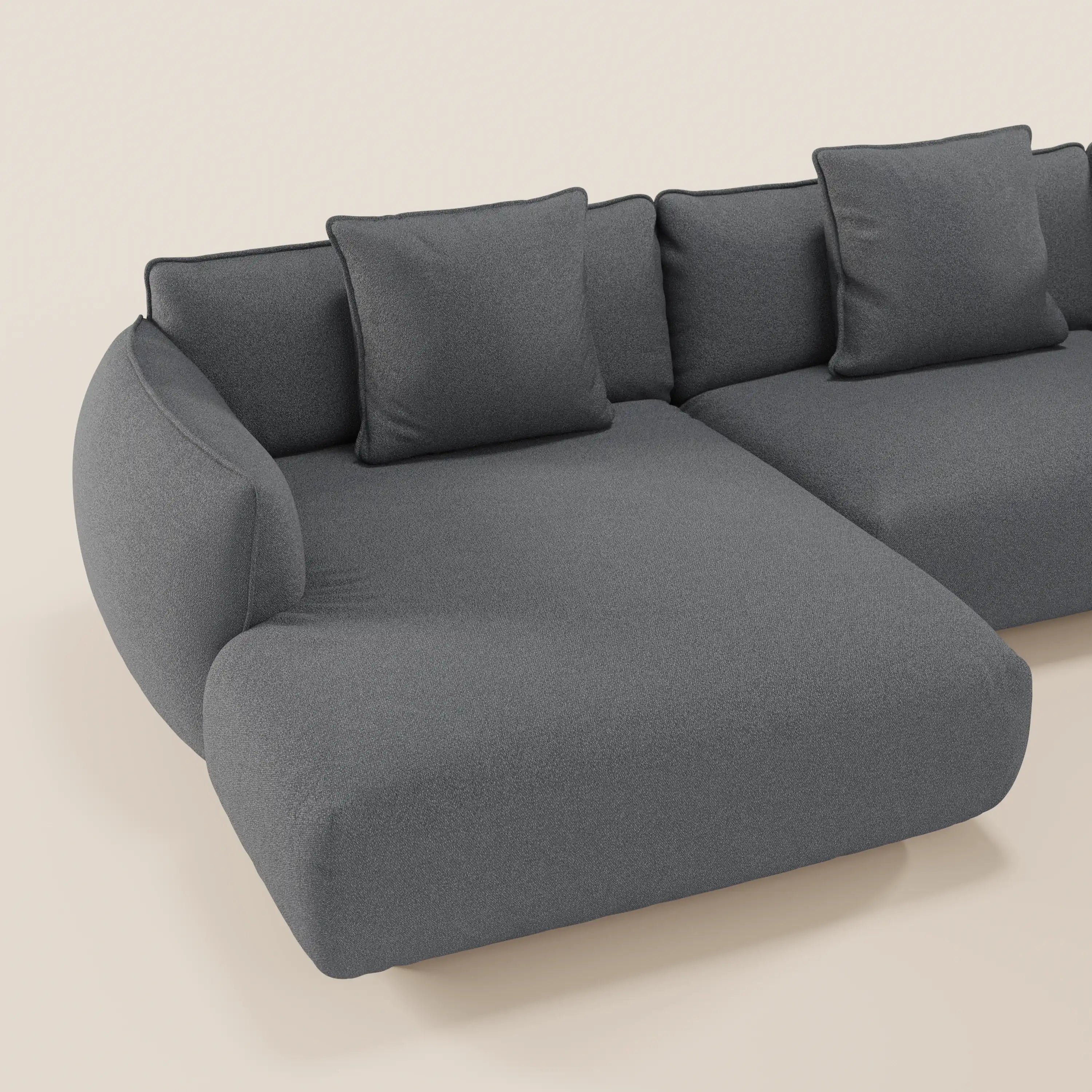Il divano Nimbus angolare panoramico componibile di Divani.Store, in tessuto antimacchia grigio scuro t33, è caratterizzato da bordi minimalisti e arrotondati e da tre cuscini di schienale quadrati abbinati, su uno sfondo beige chiaro. Prodotto in Italia.