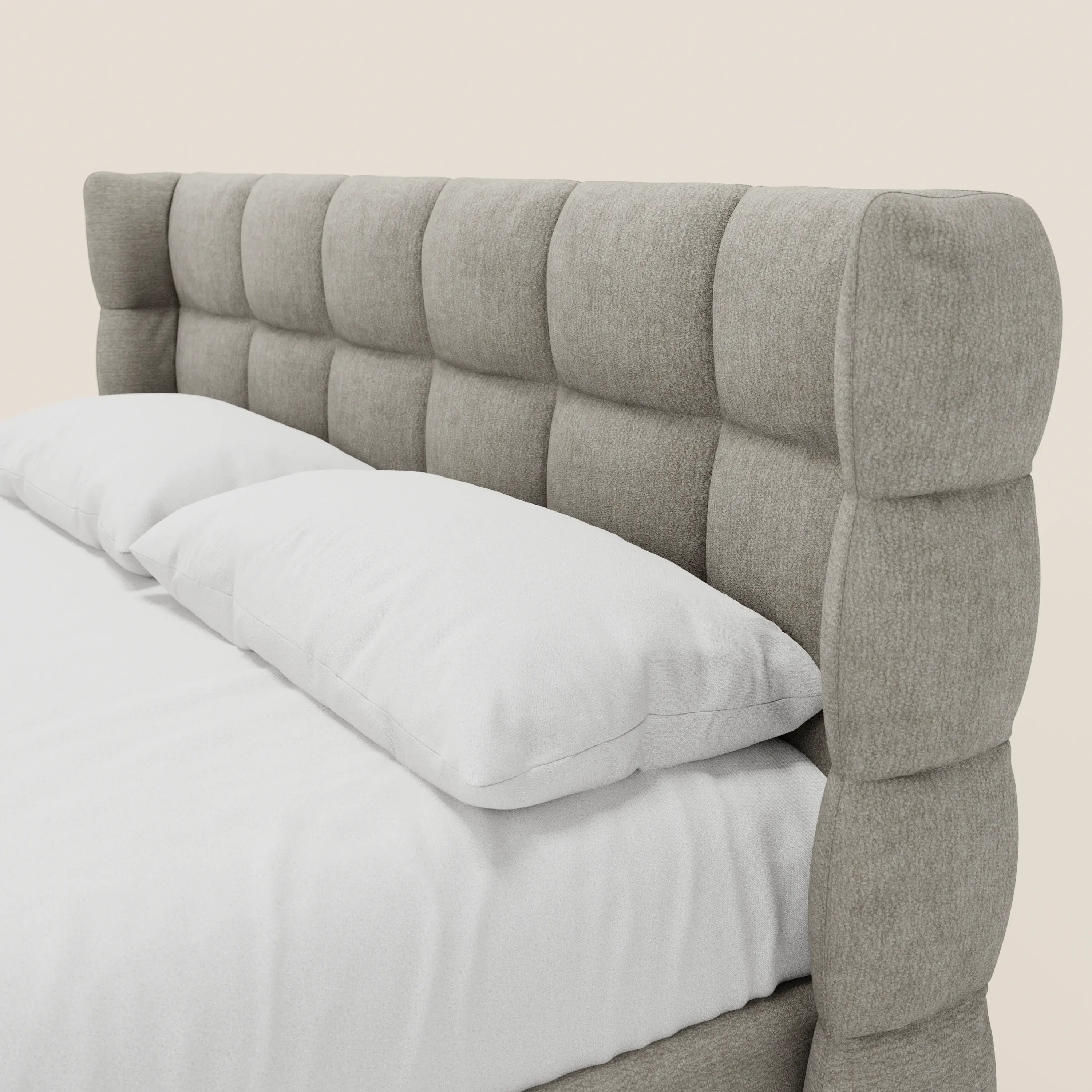 Un primo piano del letto imbottito RAGNAR con contenitore e testiera capitonné avvolgente di Letti.store, realizzato in elegante tessuto Oeko-Tex®, con lenzuolo bianco e due morbidi cuscini, per uno stile minimalista e accogliente.