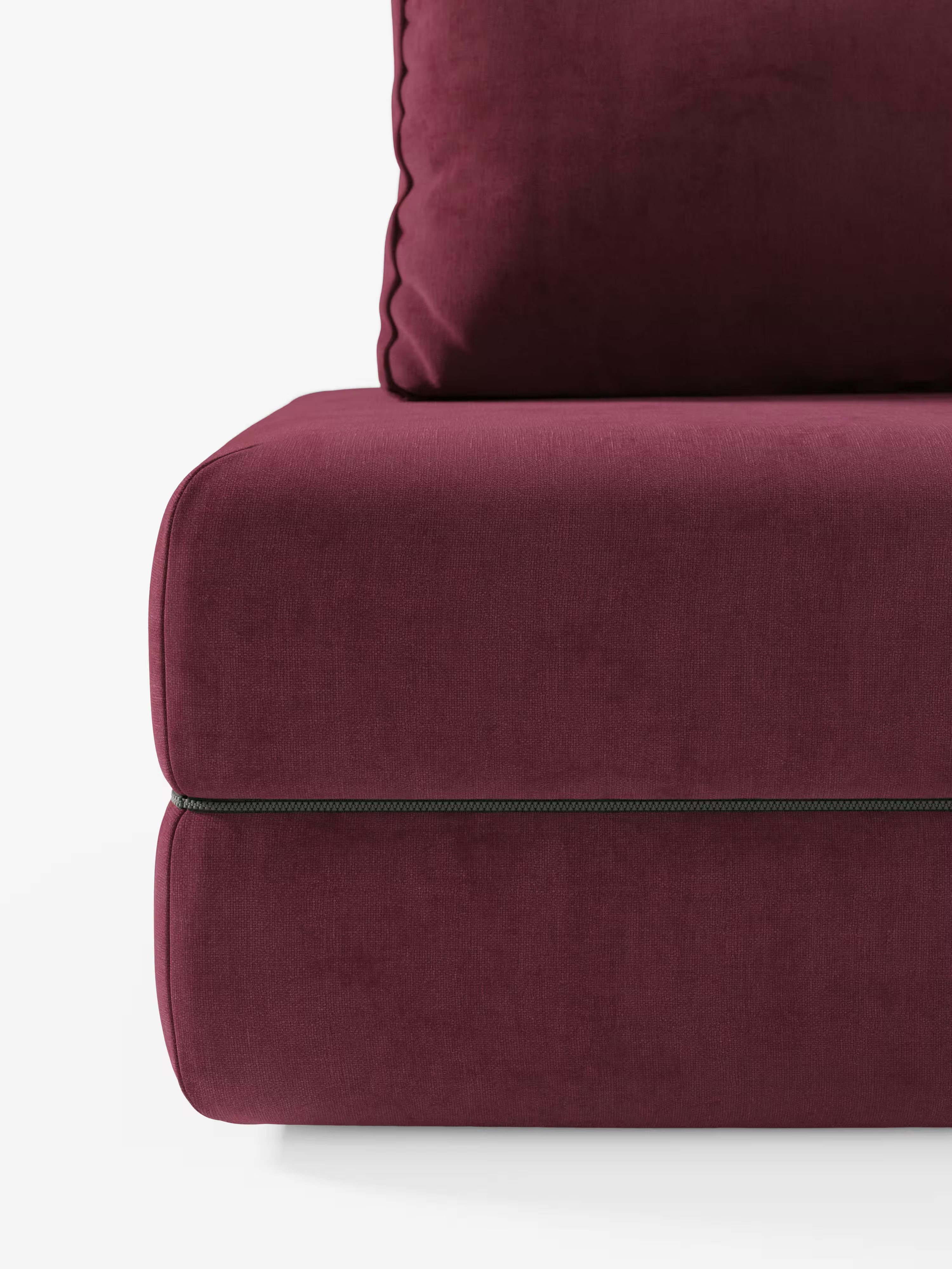Primo piano di un cuscino imbottito color bordeaux con una cucitura a cerniera nera a vista che separa due sezioni, sormontato da un cuscino dello schienale abbinato, anch’esso bordeaux, rifinito con bordino a passamaneria — il tutto su uno sfondo bianco. Questo elegante dettaglio proviene dal divano letto matrimoniale Rift a 2 e 3 posti con schienali mobili di Divani.Store, dotato di un materasso in memory foam alto 24 cm rivestito in tessuto T31 antimacchia.