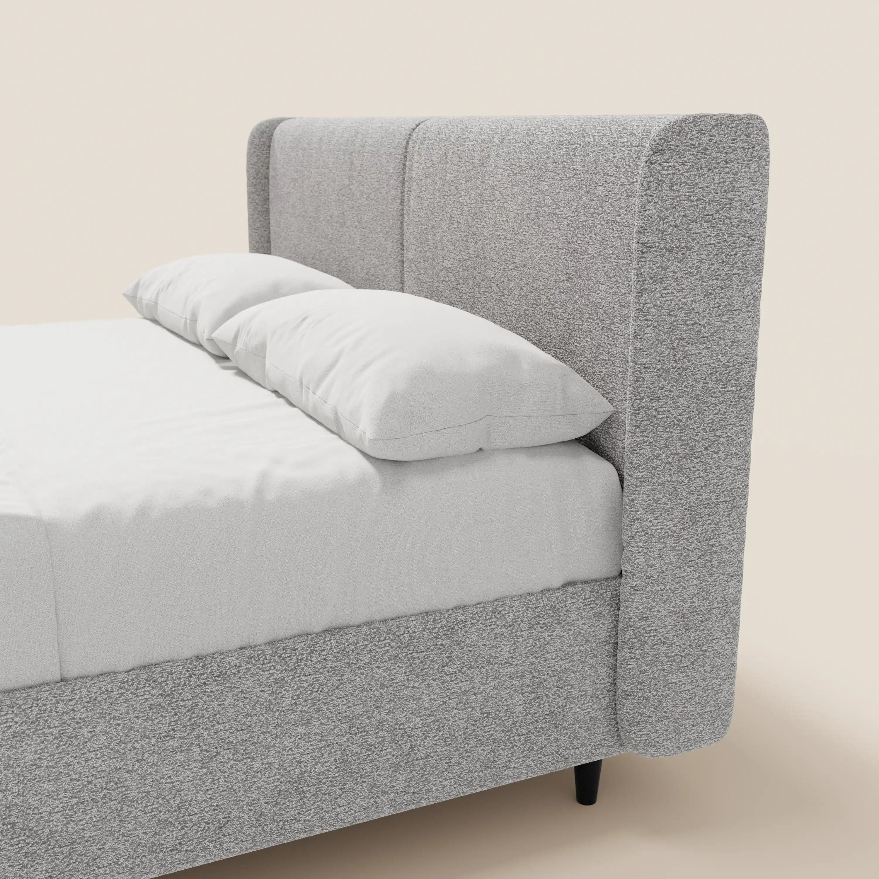 Il letto di design VALKIRIA di Letti.store presenta una struttura in tessuto grigio chiaro certificato Oeko-Tex®, due cuscini imbottiti e una testiera avvolgente. Su uno sfondo beige a tinta unita è visibile solo il lato destro di questo moderno letto contenitore.