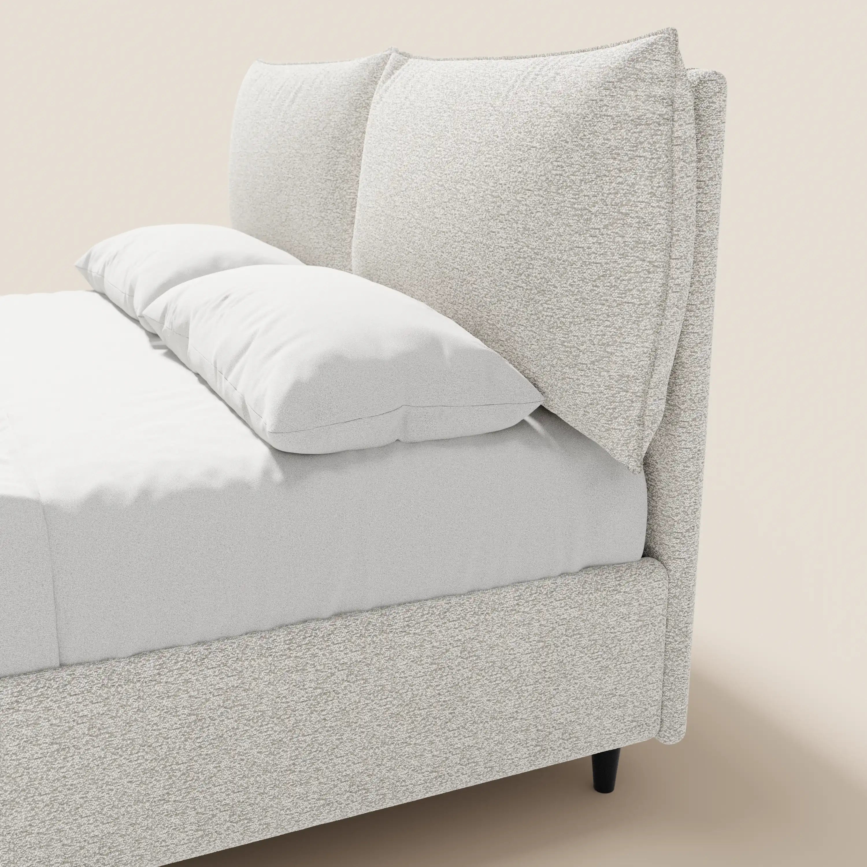 Un primo piano di ZAYRON di Letti.store: un letto imbottito in stile moderno con vano contenitore, morbidi cuscini regolabili in tessuto certificato Oeko-Tex®, biancheria da letto candida e gambe sottili scure che risaltano su uno sfondo neutro.