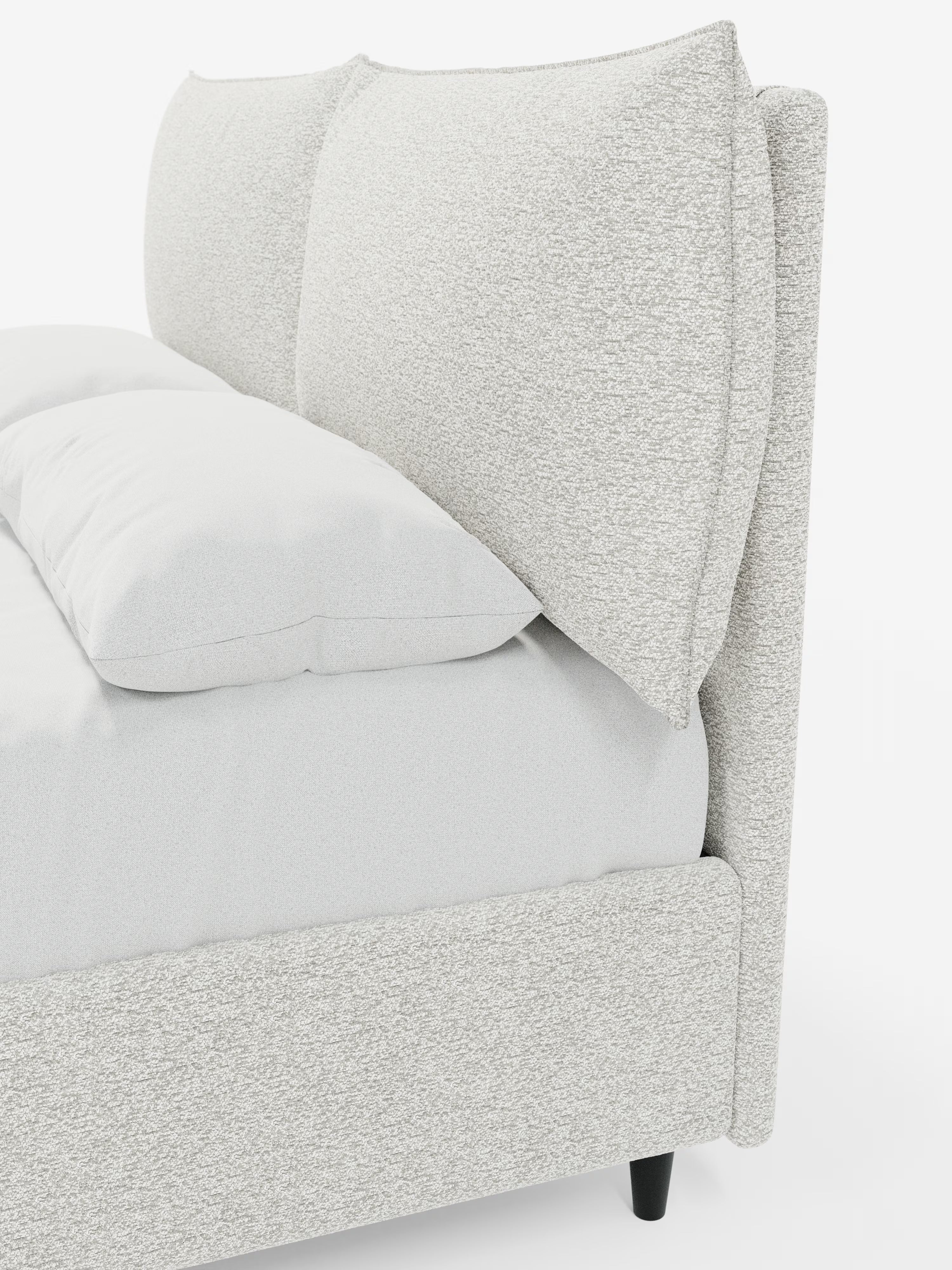 Un primo piano del letto imbottito ZAYRON con contenitore e morbidi cuscini regolabili di Letti.store, caratterizzato da un design moderno in tessuto grigio chiaro testurizzato certificato Oeko-Tex®. Il letto presenta due grandi cuscini morbidi e regolabili che fungono da testiera e una biancheria da letto di un bianco candido. È inclinato in modo da mostrare sia il lato che una parte della parte anteriore, con brevi gambe nere visibili sotto la struttura imbottita.