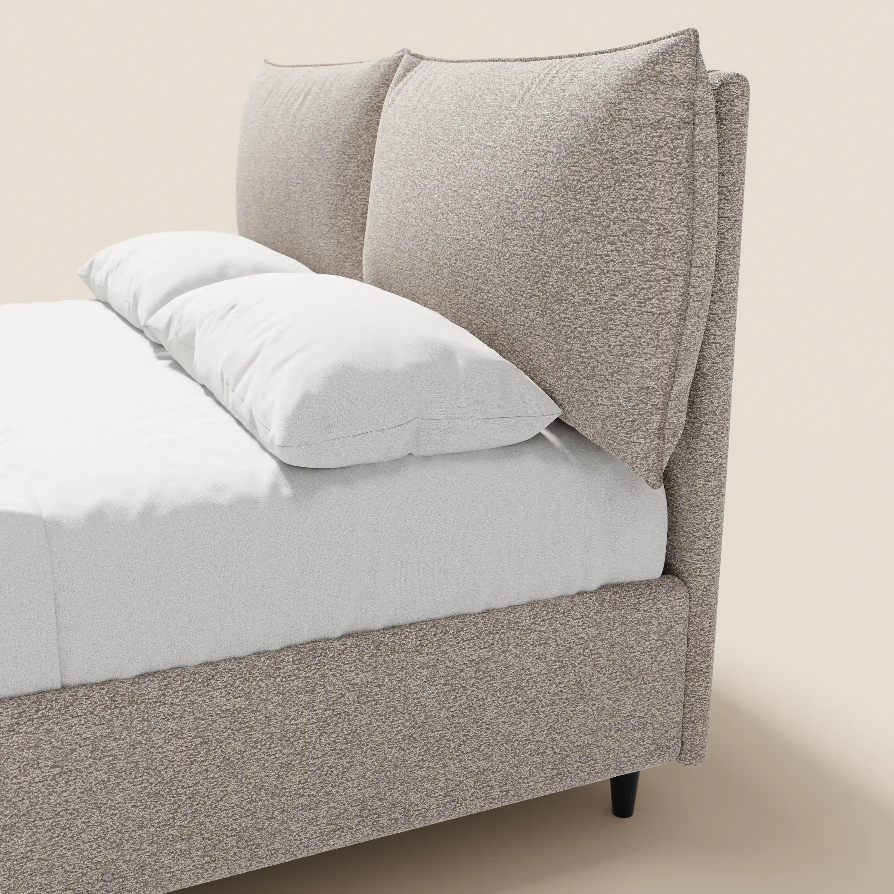 Il letto imbottito ZAYRON di Letti.store presenta una moderna struttura in tessuto beige certificata Oeko-Tex®, un ampio vano contenitore, morbidi cuscini regolabili per la testiera, biancheria da letto bianca e gambe affusolate nere che risaltano sullo sfondo beige chiaro.