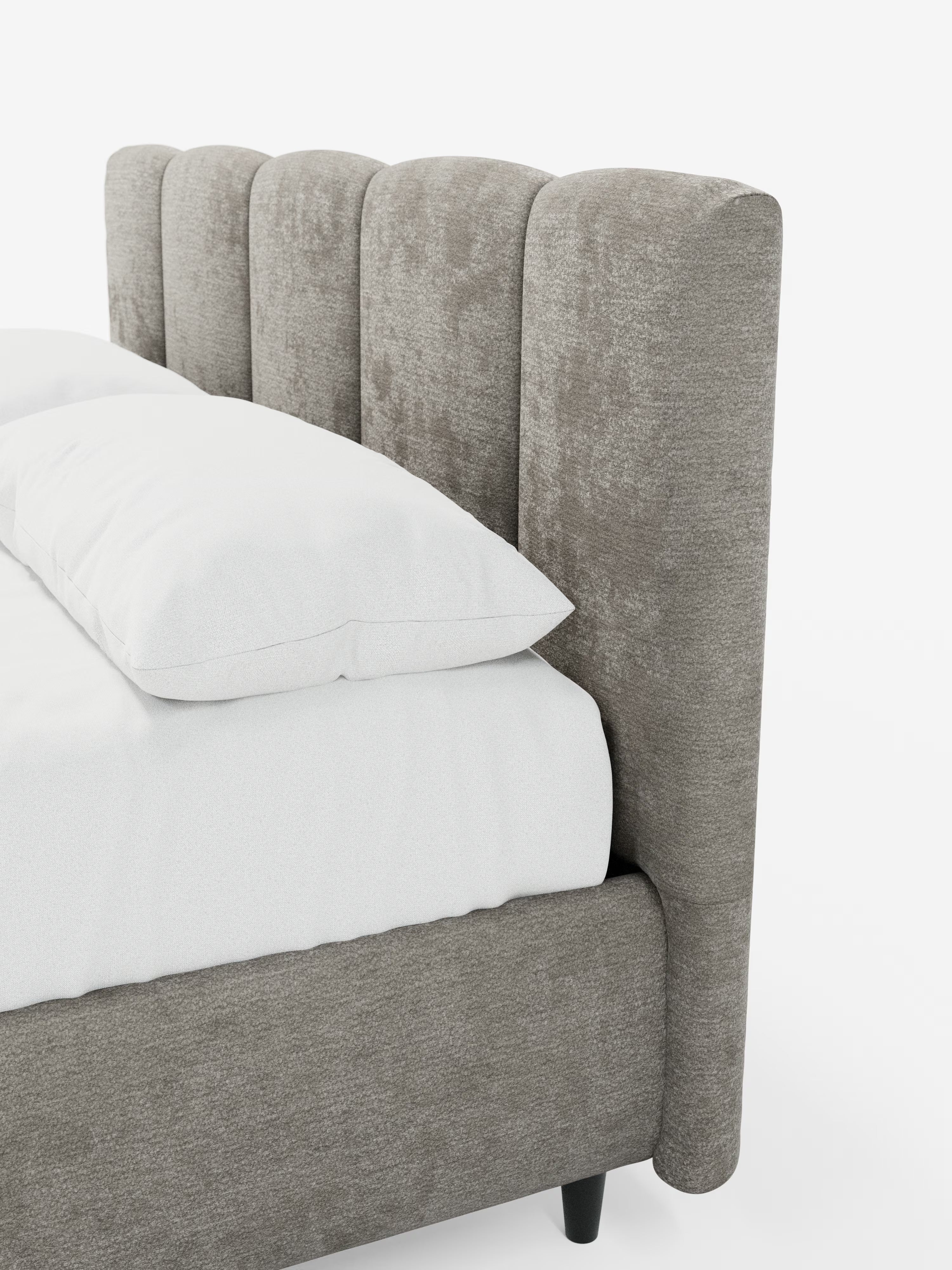Un primo piano del letto imbottito ARKAM con contenitore e testiera a lavorazione verticale di Letti.store, caratterizzato da una testiera alta, con scanalature verticali, di colore grigio chiaro, imbottita in tessuto certificato Oeko-Tex®. Il materasso è rivestito con biancheria da letto e cuscini bianchi. Questo letto in stile shabby chic comprende una struttura imbottita abbinata con gambe corte e scure. Il tutto su uno sfondo bianco a tinta unita.