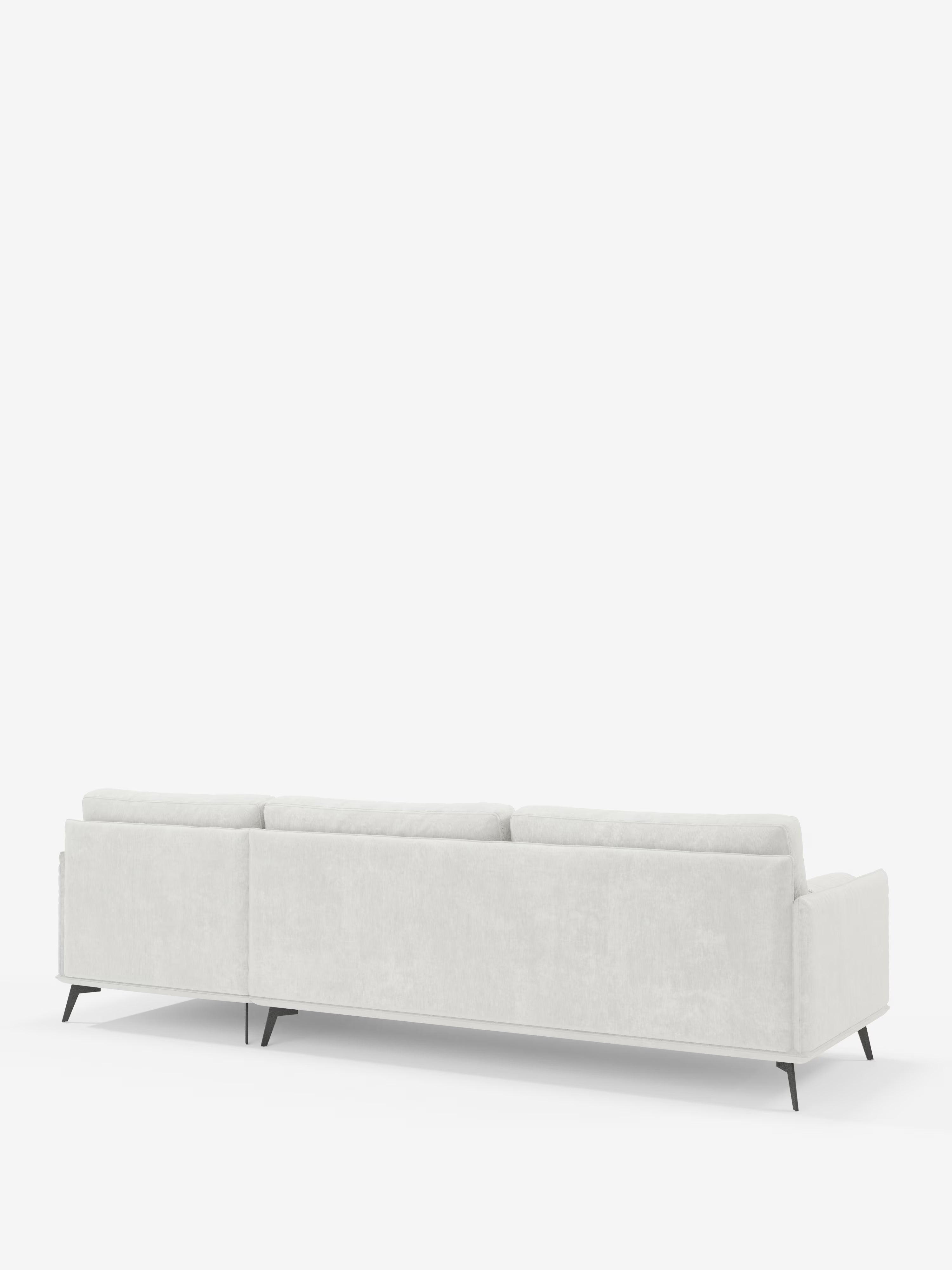 Il divano moderno angolare con penisola Basalto di Divani.Store è ripreso dal retro su uno sfondo bianco a tinta unita. Questo elegante divano italiano presenta tre schienali, linee pulite e sottili gambe angolari in metallo nero, per un’estetica minimalista. Rivestito in tessuto T31 grigio chiaro antimacchia e dotato di morbidi cuscini in piuma, il suo design elegante e contemporaneo incarna alla perfezione la raffinata maestria artigianale del Made in Italy.