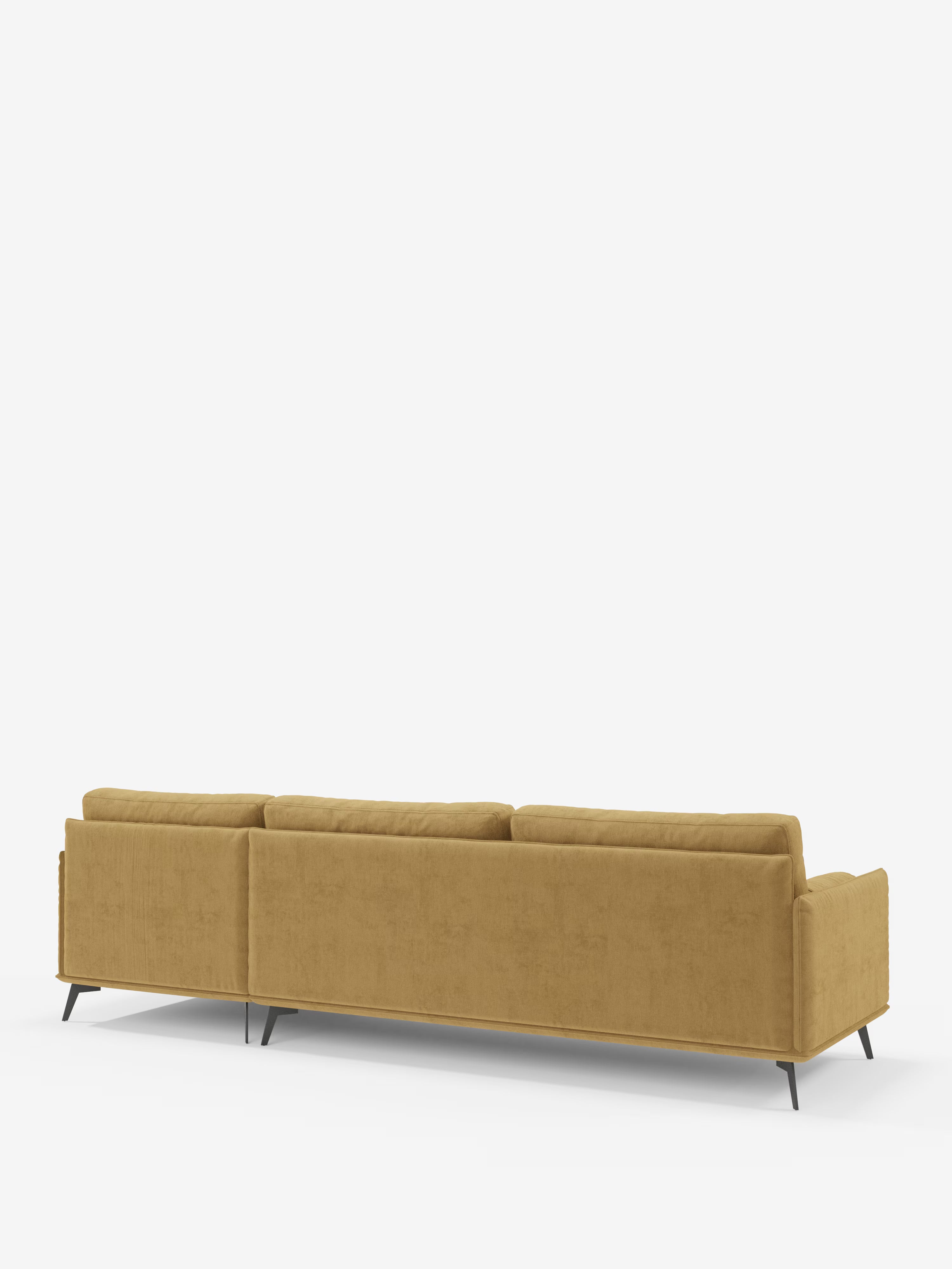 Un divano moderno angolare con penisola "Basalto" di Divani.Store, color giallo senape, è ripreso da dietro: presenta cuscini squadrati imbottiti di piume in tessuto T31 antimacchia, una silhouette elegante e minimalista e una base sottile in metallo nero su uno sfondo bianco a tinta unita.