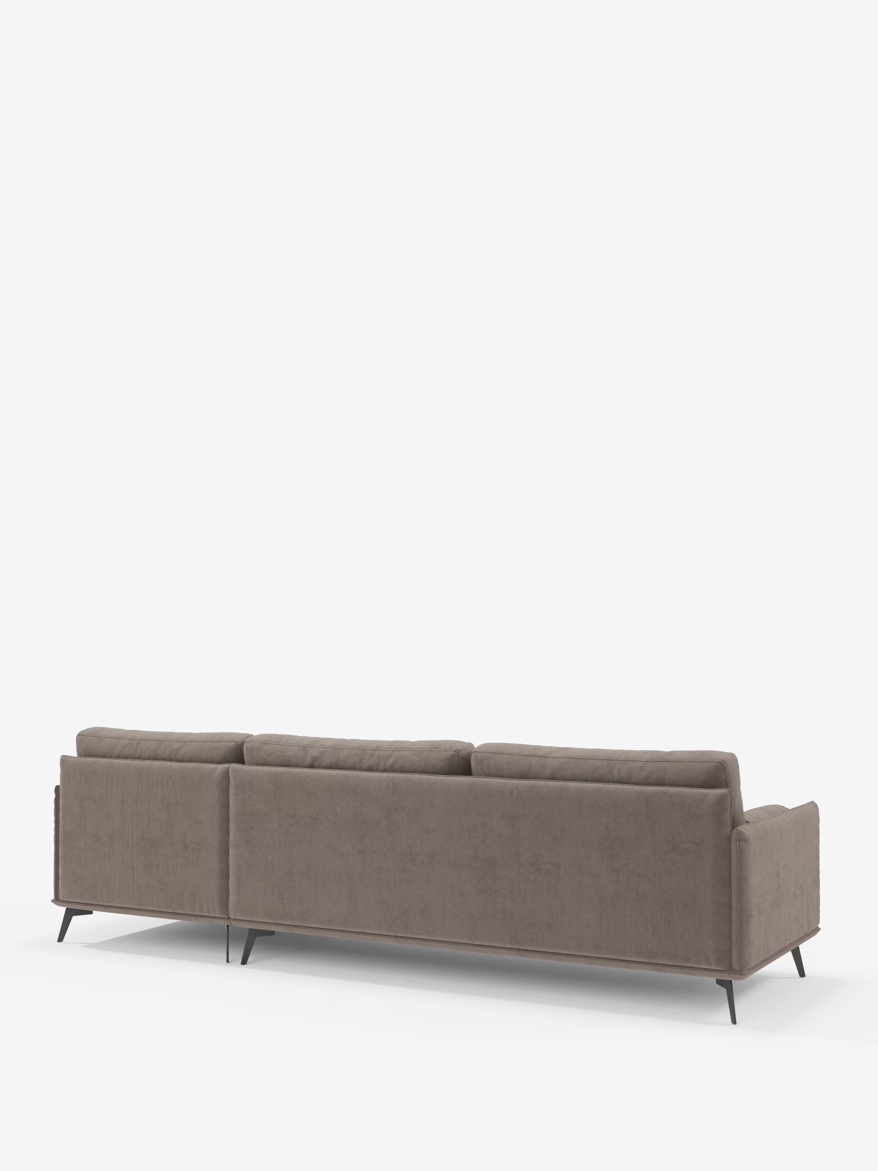 Il divano moderno angolare con penisola Basalto di Divani.Store è ripreso nella vista posteriore. Questo divano italiano contemporaneo, realizzato con tessuto T31 marrone chiaro resistente alle macchie e cuscini in piuma, presenta braccioli bassi e tre cuscini dello schienale. È sostenuto da un'elegante base in metallo con sottili gambe nere, che risalta su uno sfondo bianco a tinta unita.