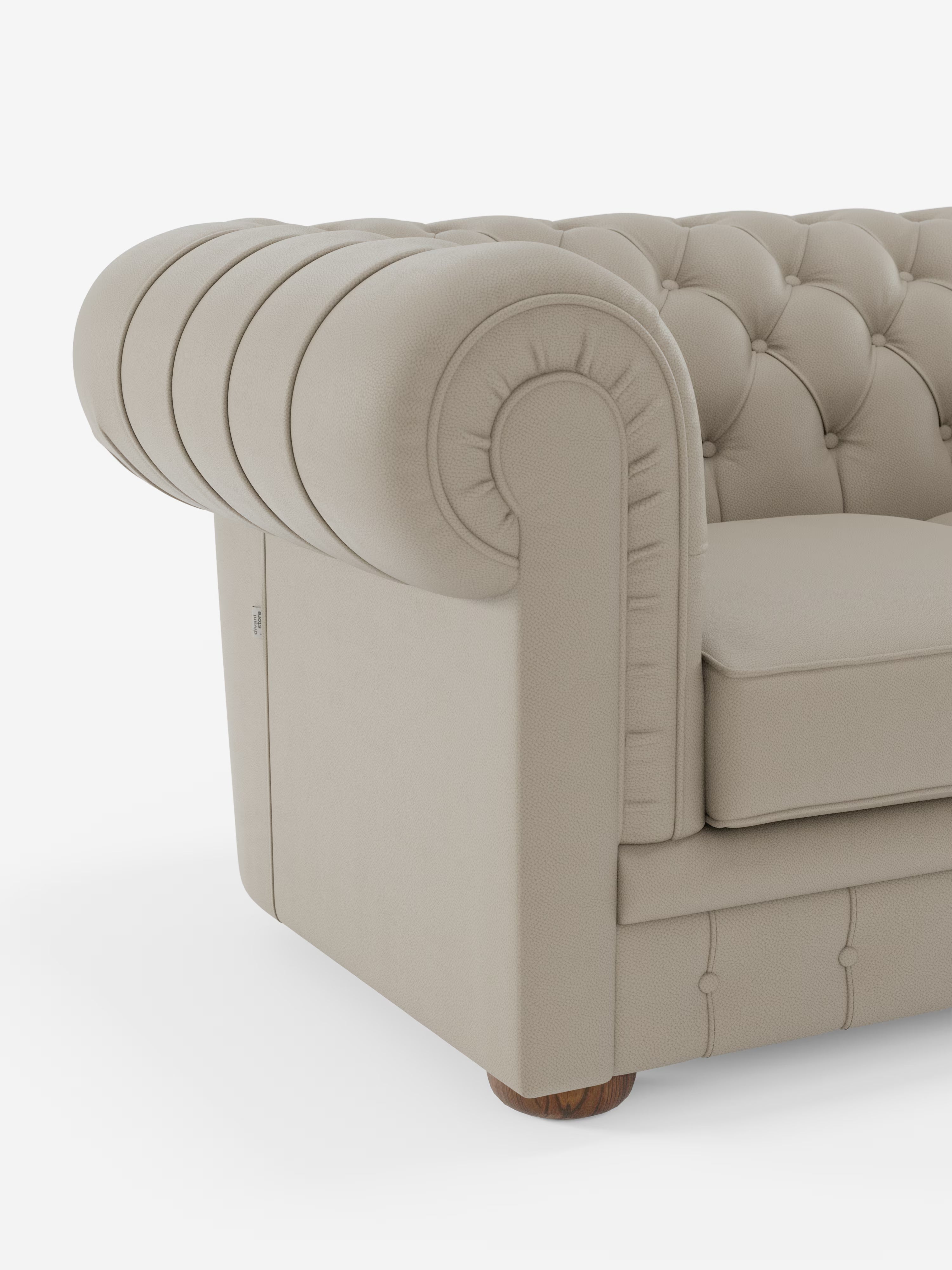 Primo piano della vista laterale del Divani.Store Chester 4 Posti 3 sedute in Vera Pelle – Chesterfield Capitonné Artigianale, caratterizzato da rivestimento in vera pelle liscia beige, classici braccioli arrotondati, trapuntatura a bottoni e gambe in legno. Il cuscino di seduta, rigido e spesso, mette in risalto la raffinata lavorazione artigianale su uno sfondo bianco a tinta unita.