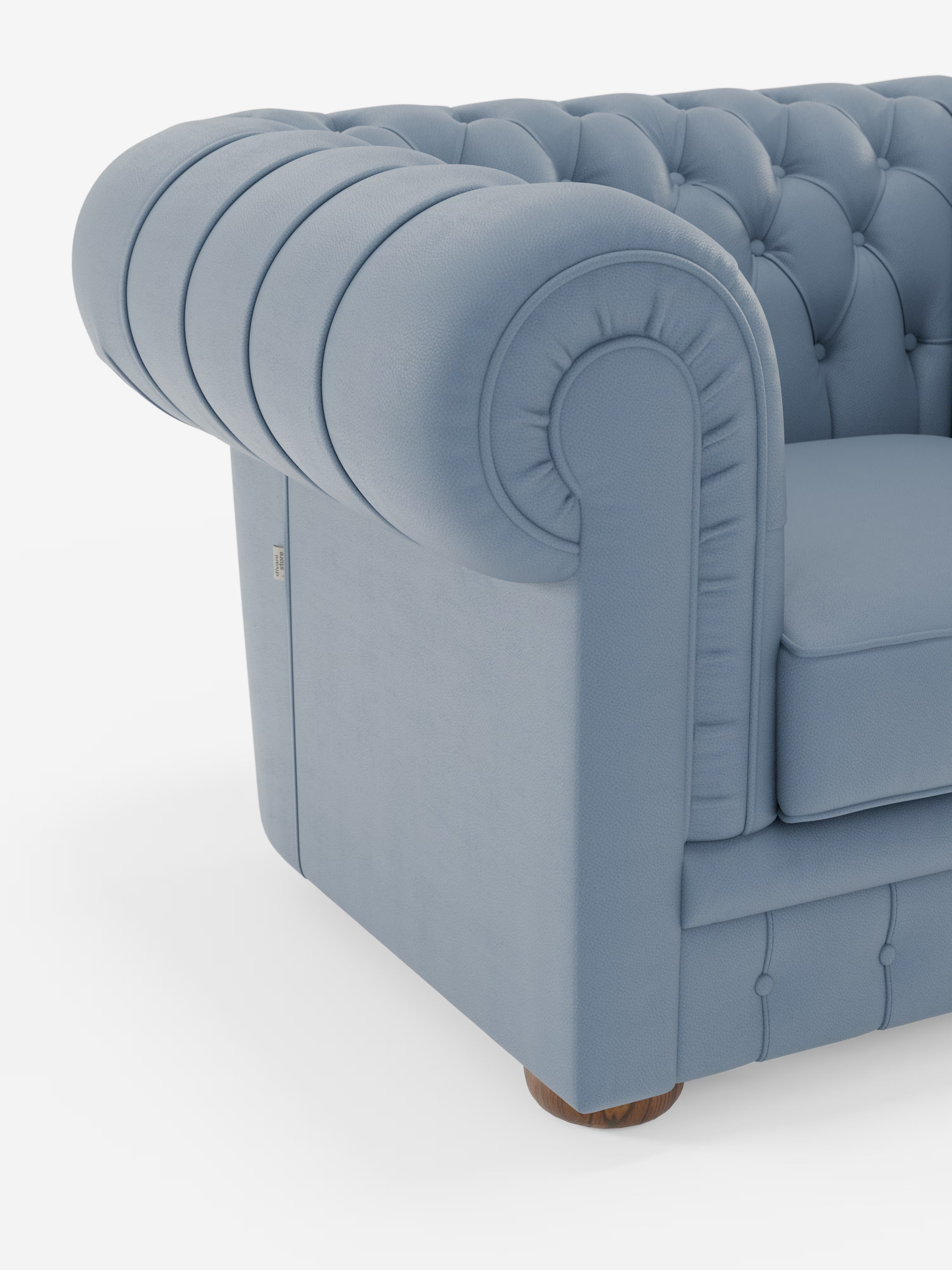 Un primo piano della poltrona Chester in vera pelle spessorata con capitonné artigianale di Divani.Store mette in risalto i braccioli arrotondati, la profonda trapuntatura a bottoni e il rivestimento testurizzato che richiama il classico design Chesterfield. La gamba in legno parzialmente visibile nella parte inferiore e lo sfondo bianco a tinta unita accentuano il lusso raffinato di questo elemento d’arredo artigianale.