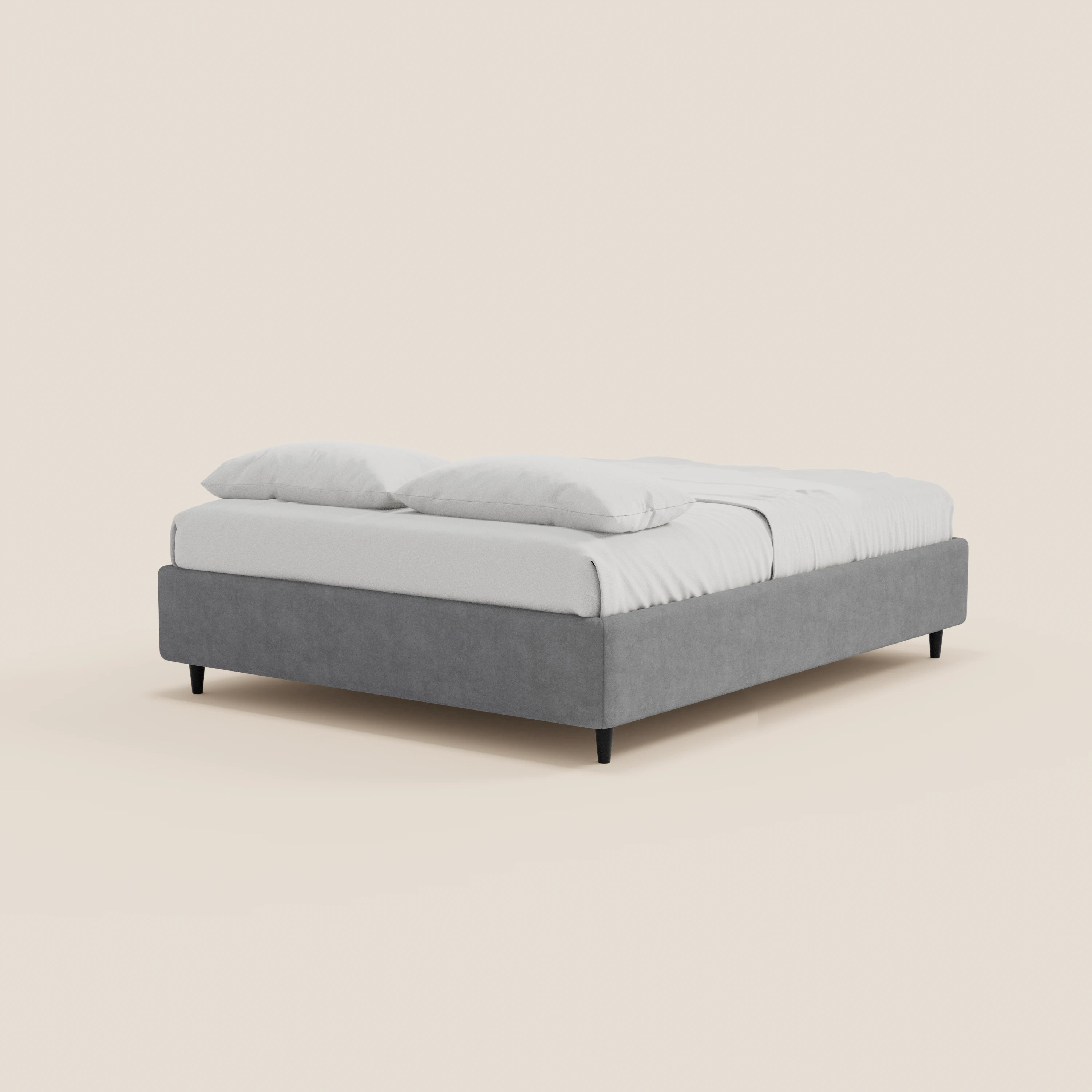 Il letto sommier imbottito ERON di Letti.store è caratterizzato da un tessuto grigio impermeabile certificato Oeko-Tex, una struttura rettangolare bassa, gambe sottili nere e un vano contenitore, con biancheria da letto e cuscini bianchi che risaltano su uno sfondo beige chiaro.