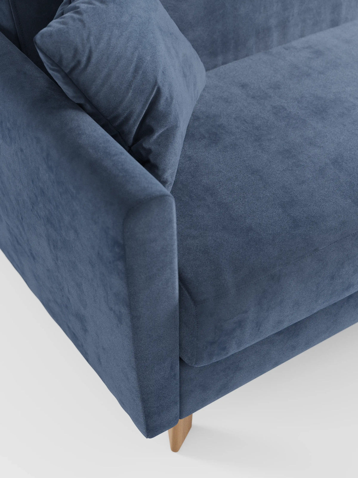 Primo piano di un divano letto Francy con poggiatesta regolabili di Divani.Store, rivestito in morbido tessuto blu T30 resistente alle macchie. L’immagine mette in risalto il bracciolo, un cuscino coordinato e parte della seduta, evidenziando le linee pulite del divano e le gambe in legno chiaro su uno sfondo bianco a tinta unita. Il rivestimento è interamente sfoderabile per facilitare la pulizia.