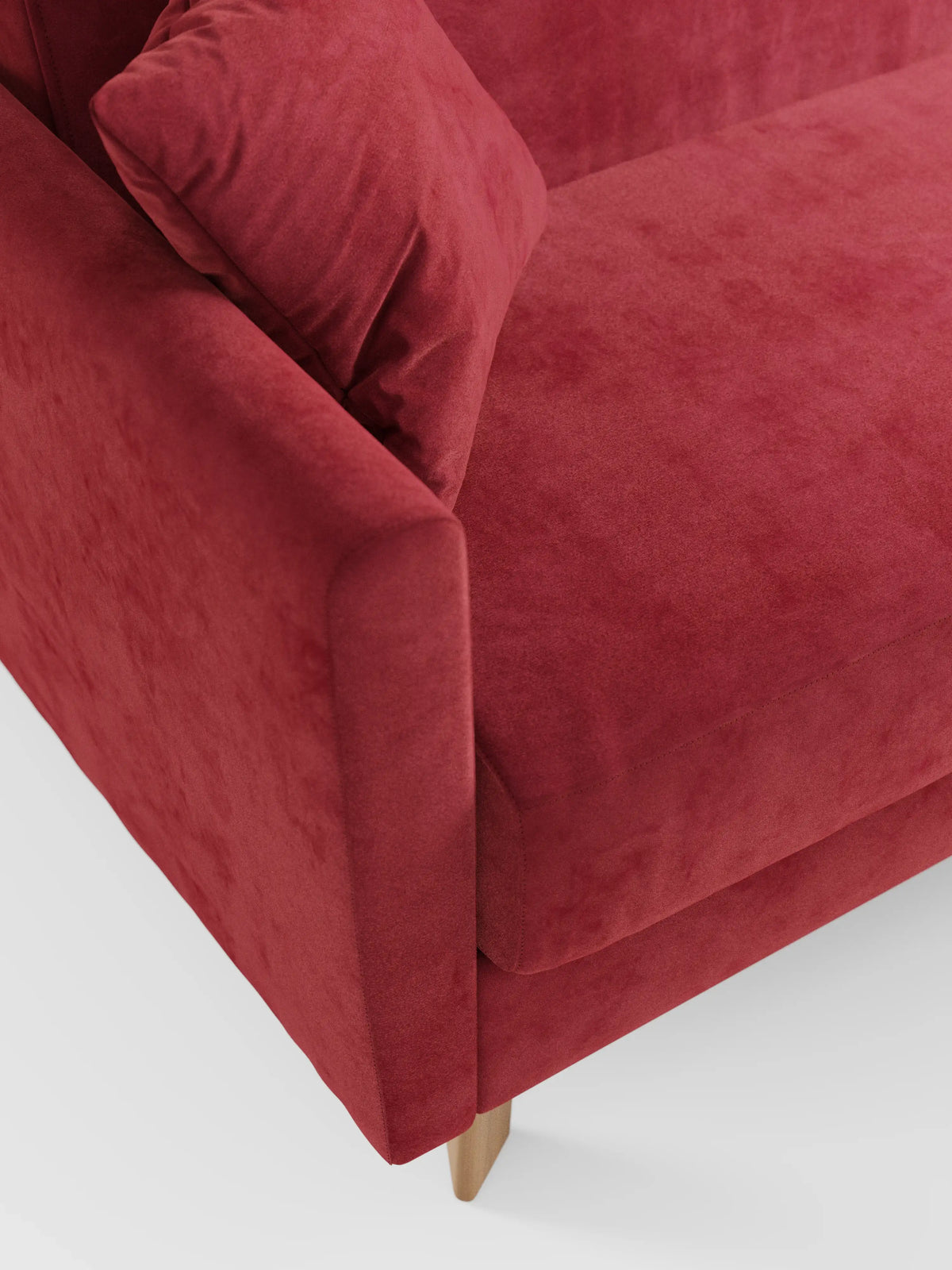 Un primo piano del divano letto Francy con poggiatesta regolabili di Divani.Store in un rosso accattivante, con un cuscino abbinato che mette in risalto i braccioli angolati, la seduta e le gambe in legno. Il rivestimento è realizzato in elegante tessuto T30 resistente alle macchie, dall’aspetto morbido e dalla texture simile alla pelle scamosciata. Lo sfondo è una superficie bianca a tinta unita.