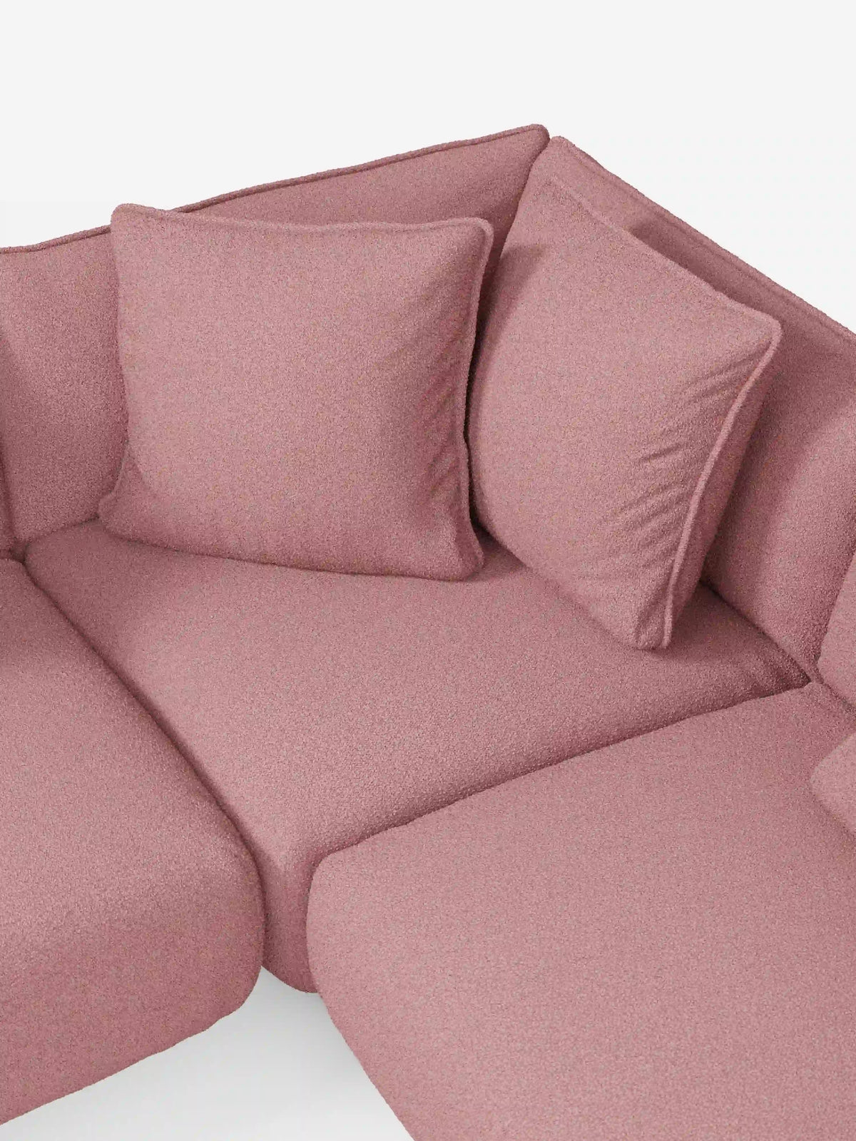 Un primo piano del divano angolare panoramico componibile Nimbus con penisola e angolo in tessuto smacchiabile T33 di Divani.Store mette in risalto il suo tessuto morbido, strutturato e resistente alle macchie, in colore rosa. Il divano componibile presenta due grandi cuscini coordinati, disposti ordinatamente nell’angolo contro lo schienale. Le linee pulite e il design moderno sottolineano l’eccezionale qualità e l’artigianalità italiana che contraddistinguono i mobili Divani.Store.