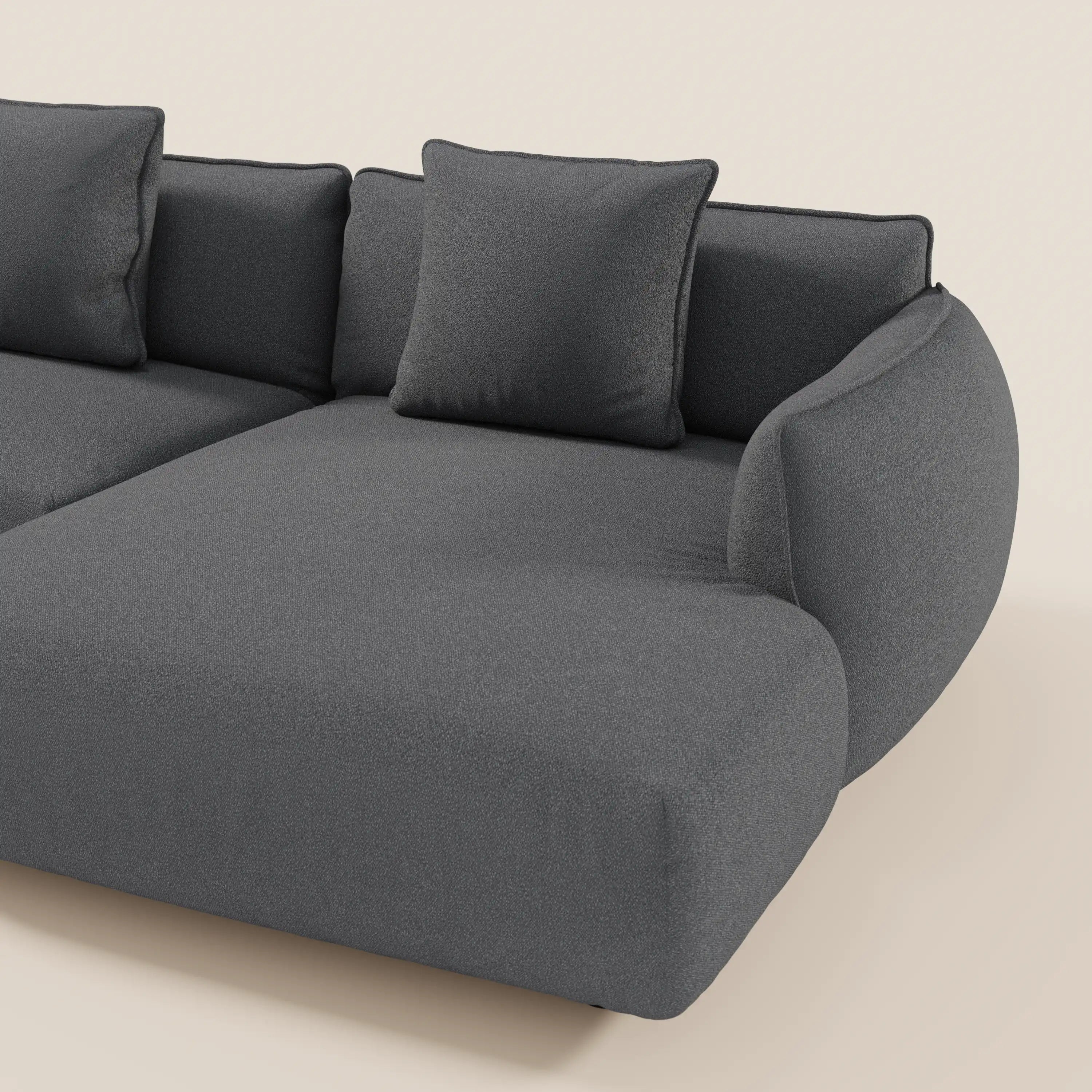 Il divano Nimbus angolare con penisola componibile in tessuto effetto cotone smacchiabile T33 di Divani.Store è caratterizzato da sedute ampie e morbide, braccioli arrotondati e due cuscini quadrati per lo schienale in grigio scuro su sfondo beige chiaro.