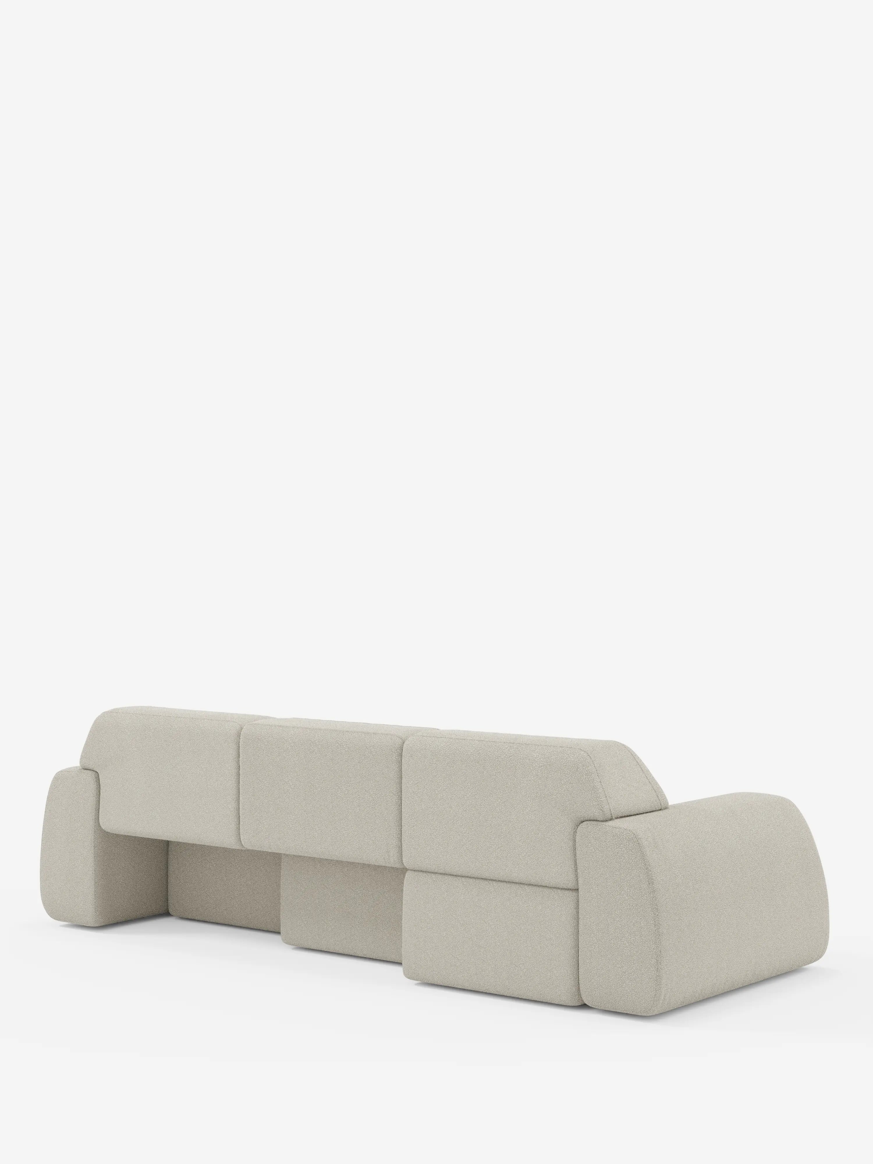 Un divano moderno e modulare color beige chiaro — il modello Orbit con 3 sedute scorrevoli e allungabili in tessuto effetto cotone smacchiabile T33 di Divani.Store — presenta bordi morbidi e arrotondati ed è raffigurato di spalle su uno sfondo bianco a tinta unita. Questo divano vanta ampi braccioli e cuciture a vista che separano ciascuna sezione imbottita, mentre il rivestimento completamente sfoderabile ne garantisce una facile pulizia e manutenzione.
