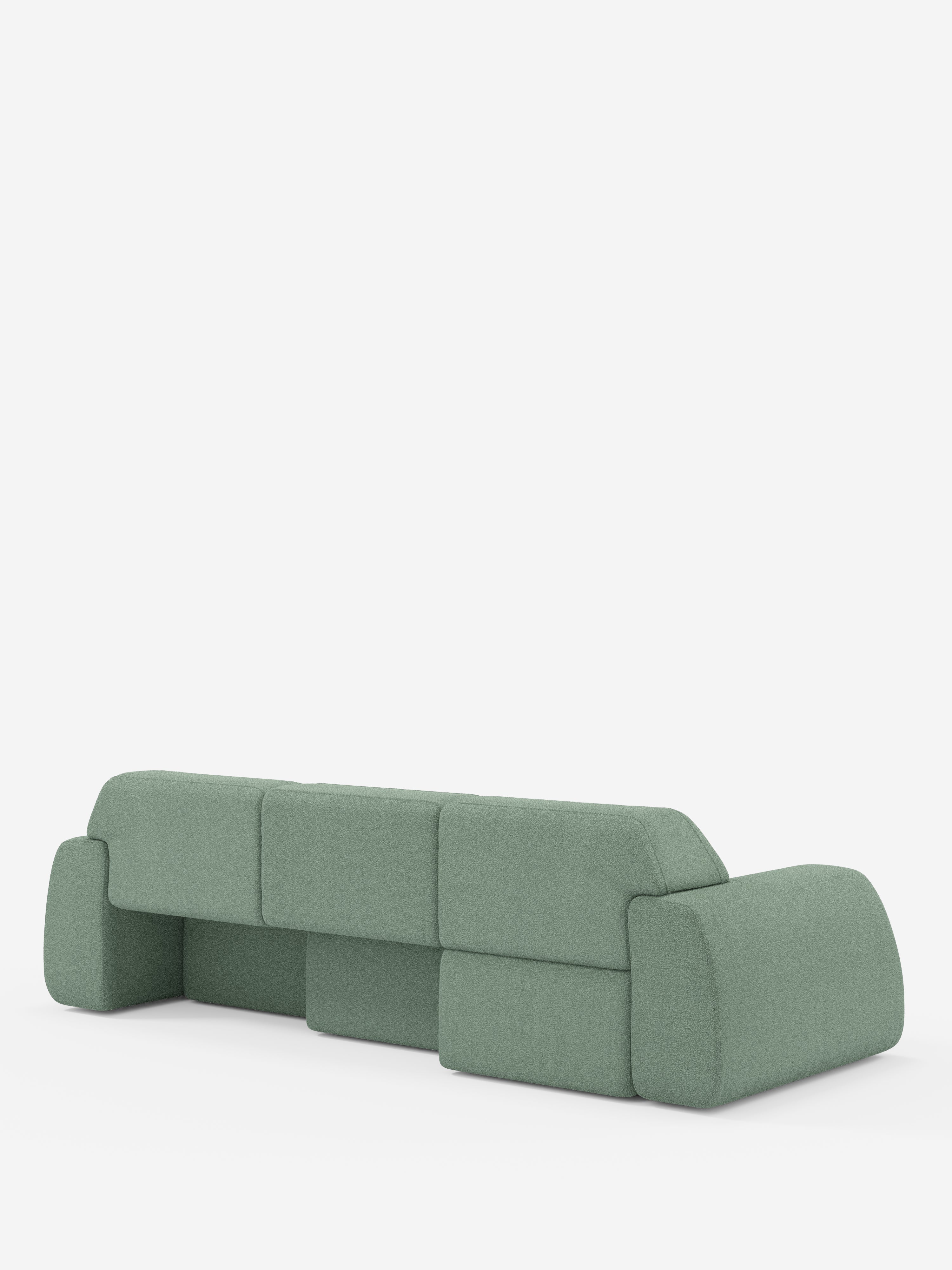 Un divano angolare Orbit verde salvia con penisola reversibile e tutte le sedute allungabili, rivestito in tessuto smacchiabile effetto cotone T33 di Divani.Store, è raffigurato al centro su uno sfondo bianco. Questo moderno divano componibile presenta bordi lisci e arrotondati, ampi braccioli, schienali bassi e un design minimalista, morbido e imbottito. La prospettiva mostra il retro e il profilo laterale del divano.