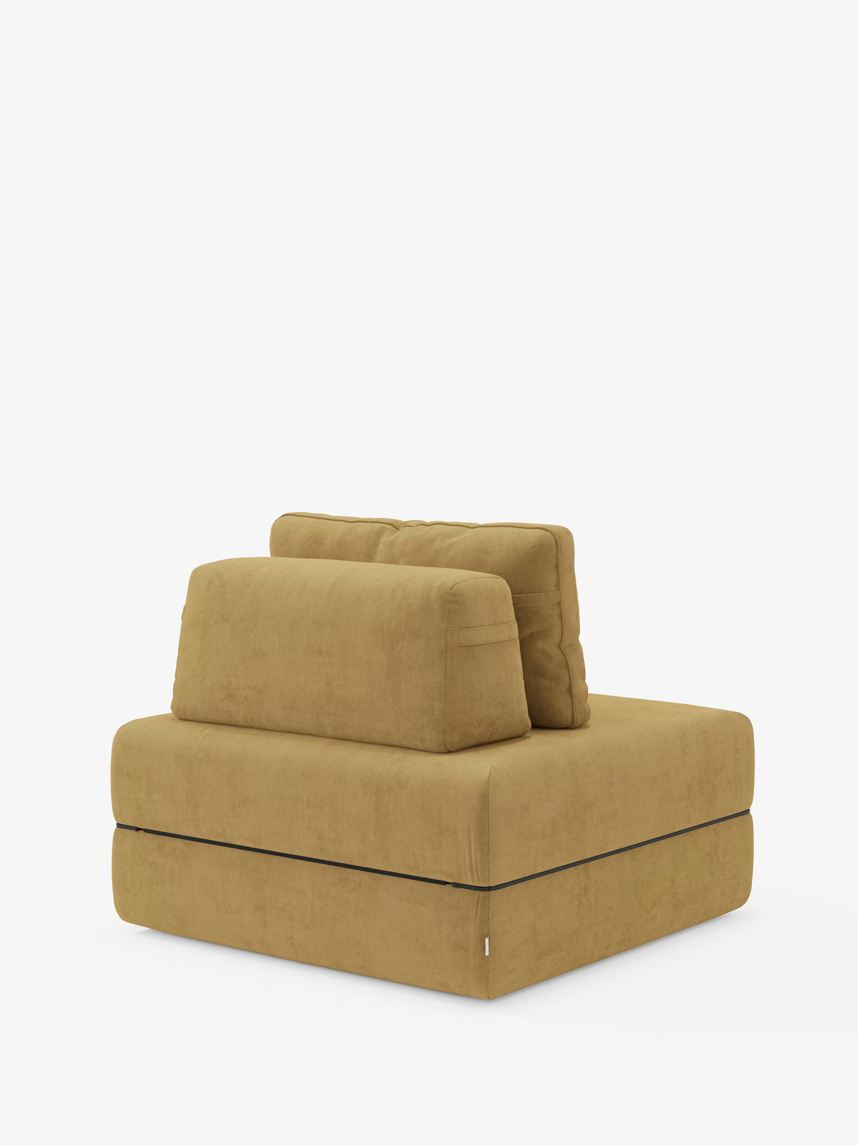 La poltrona letto Rift di Divani.Store è una moderna poltrona modulare senza braccioli, rivestita in tessuto smacchiabile T31 giallo senape. Si caratterizza per le linee pulite, due spessi cuscini di seduta rettangolari e due cuscini dello schienale rettangolari abbinati, con schienale mobile per una maggiore versatilità. La poltrona è dotata di un materasso in memory foam alto 24 cm e poggia su una base piatta con cuciture a vista, che risaltano sullo sfondo bianco.