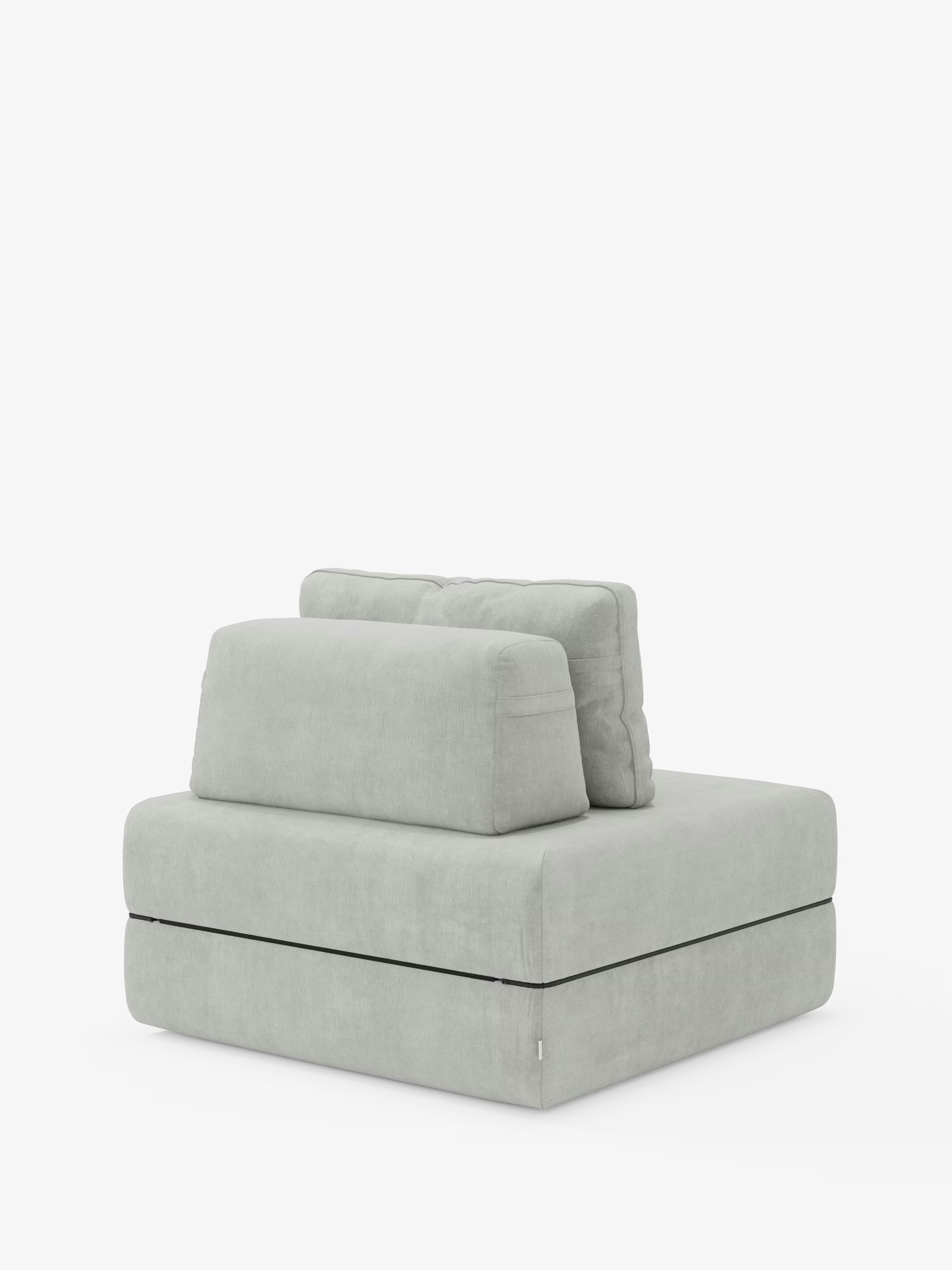 Una poltrona moderna e minimalista senza braccioli, rivestita in tessuto smacchiabile T31 grigio chiaro, con ampia seduta e due cuscini rettangolari per lo schienale, è posizionata su uno sfondo bianco a tinta unita. La poltrona letto Rift con materasso alto 24 cm e memory foam di Divani.Store si caratterizza per le linee pulite e il tessuto morbido e materico, offrendo il perfetto connubio tra stile contemporaneo e comfort accogliente grazie allo schienale mobile.