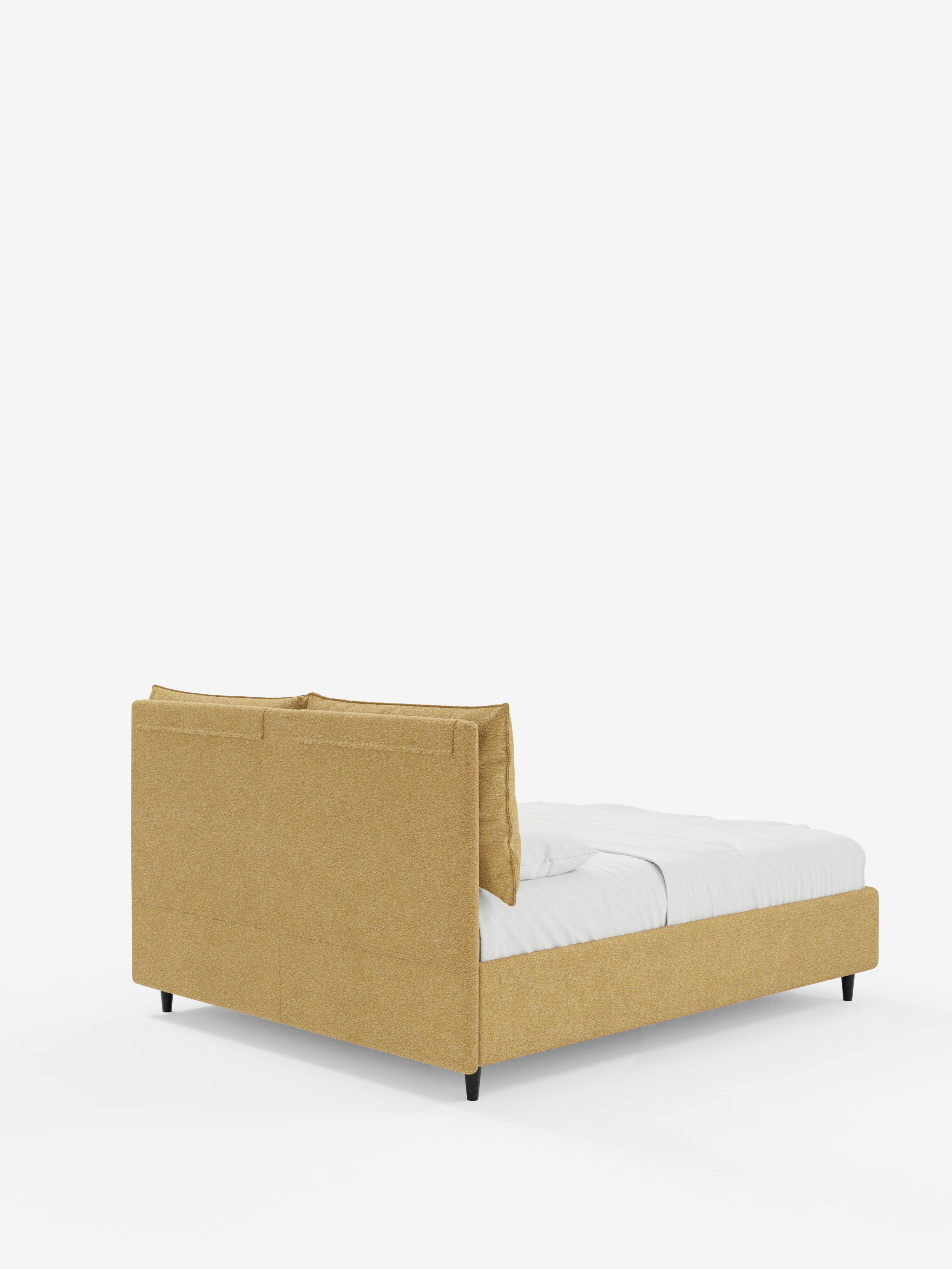 Un letto imbottito ZAYRON dal profilo basso con vano contenitore e morbidi cuscini regolabili di Letti.store, rivestito in tessuto giallo senape certificato Oeko-Tex®, visto dal retro a sinistra. Questo letto moderno presenta testiera e pediera imbottite, gambe nere ed è abbinato a biancheria da letto e cuscini bianchi su uno sfondo bianco a tinta unita.