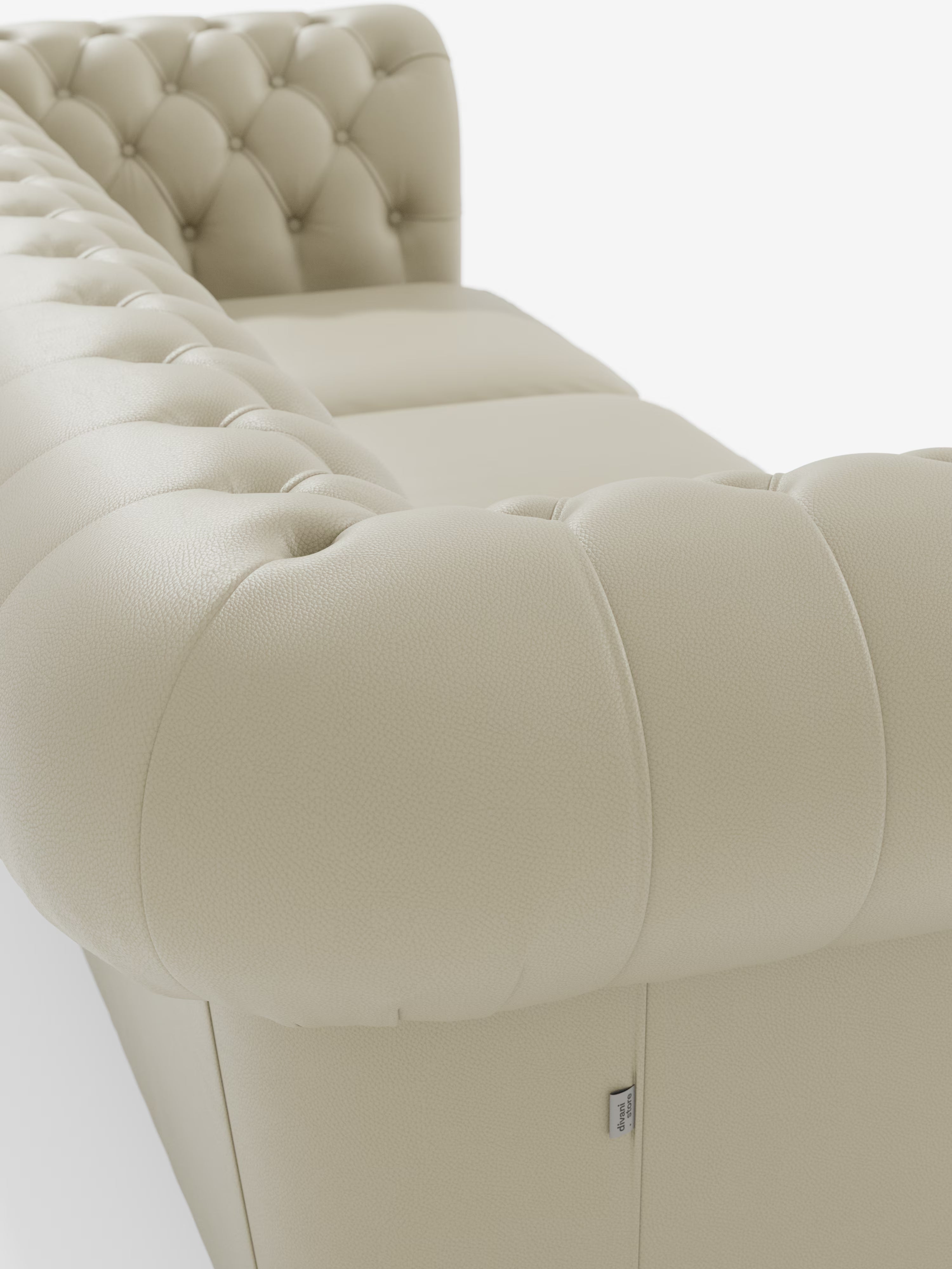 Primo piano del divano Chester 4 Posti 3 sedute in Vera Pelle – Chesterfield Capitonné Artigianale di Divani.Store, caratterizzato da un rivestimento in pelle capitonné beige e da morbidi dettagli bottonati lungo i braccioli e lo schienale, nel classico stile Chesterfield. I morbidi cuscini della seduta e una discreta etichetta in tessuto sul lato risaltano sullo sfondo bianco, sottolineandone la lavorazione artigianale.
