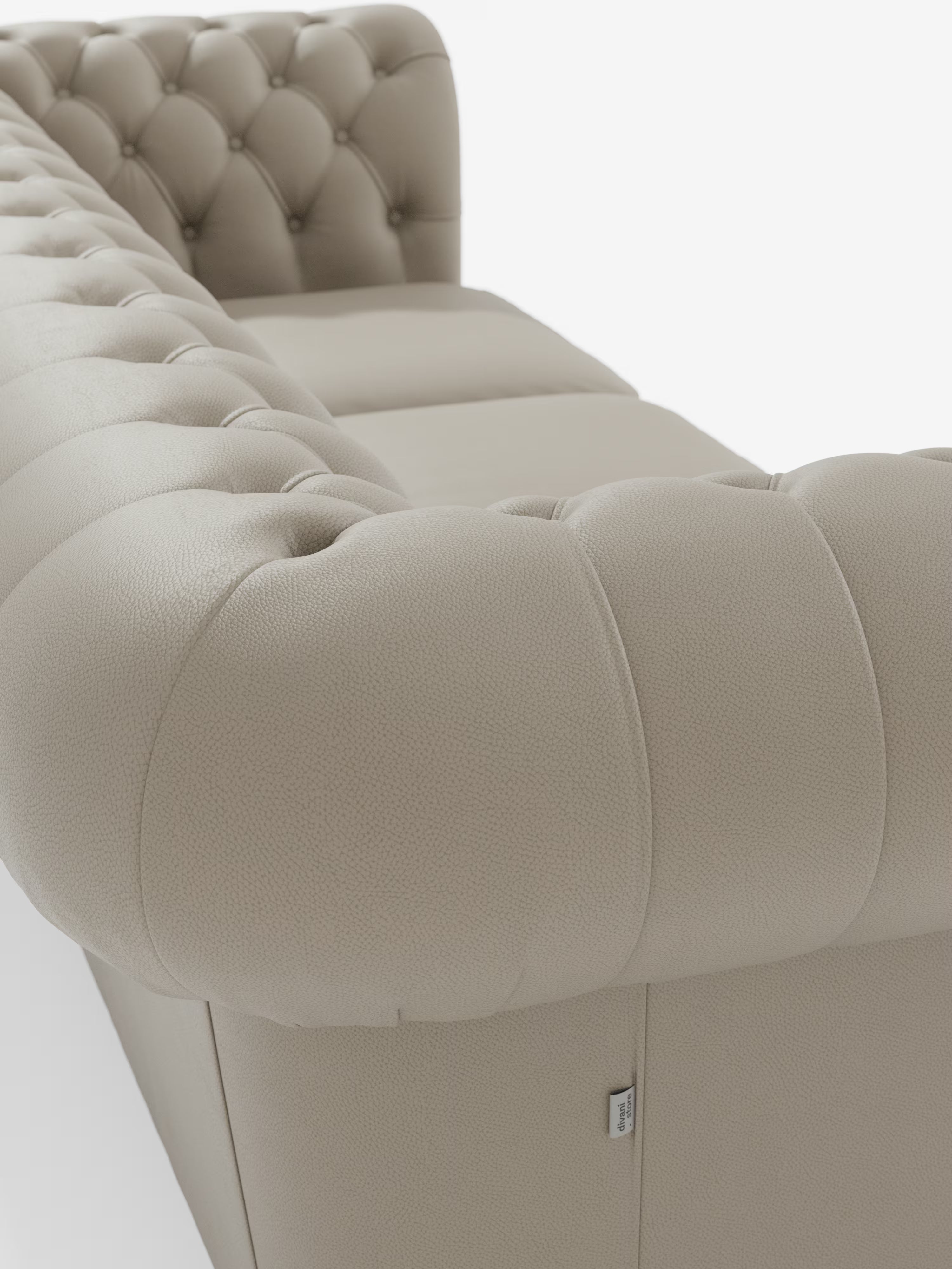 Un primo piano del divano Chester 4 Posti 3 sedute in Vera Pelle – Chesterfield Capitonné Artigianale di Divani.Store mette in risalto il rivestimento in vera pelle testurizzata e gli eleganti dettagli capitonné. Il divano beige presenta braccioli e schienale arrotondati, morbidi e imbottiti, con una piccola etichetta in tessuto visibile vicino alla base sul lato destro.