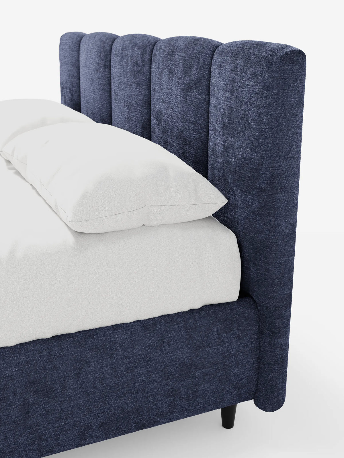 ARKAM, letto imbottito con contenitore e testiera a lavorazione verticale in blu navy scuro, caratterizzato da spesse cuciture verticali e da biancheria da letto di un bianco brillante su uno sfondo bianco a tinta unita.
