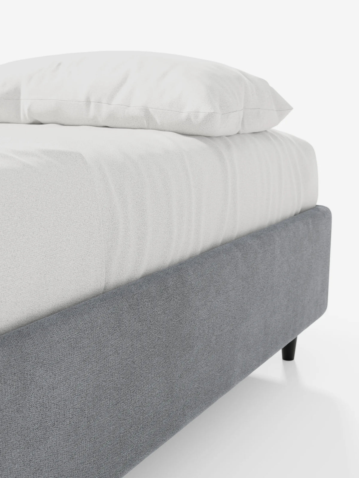 Un primo piano di un letto sommier imbottito ERON con contenitore, rivestito in tessuto impermeabile certificato Oeko-Tex in tessuto grigio testurizzato, su gambe corte e cilindriche nere, con lenzuolo bianco e cuscino su uno sfondo bianco a tinta unita.