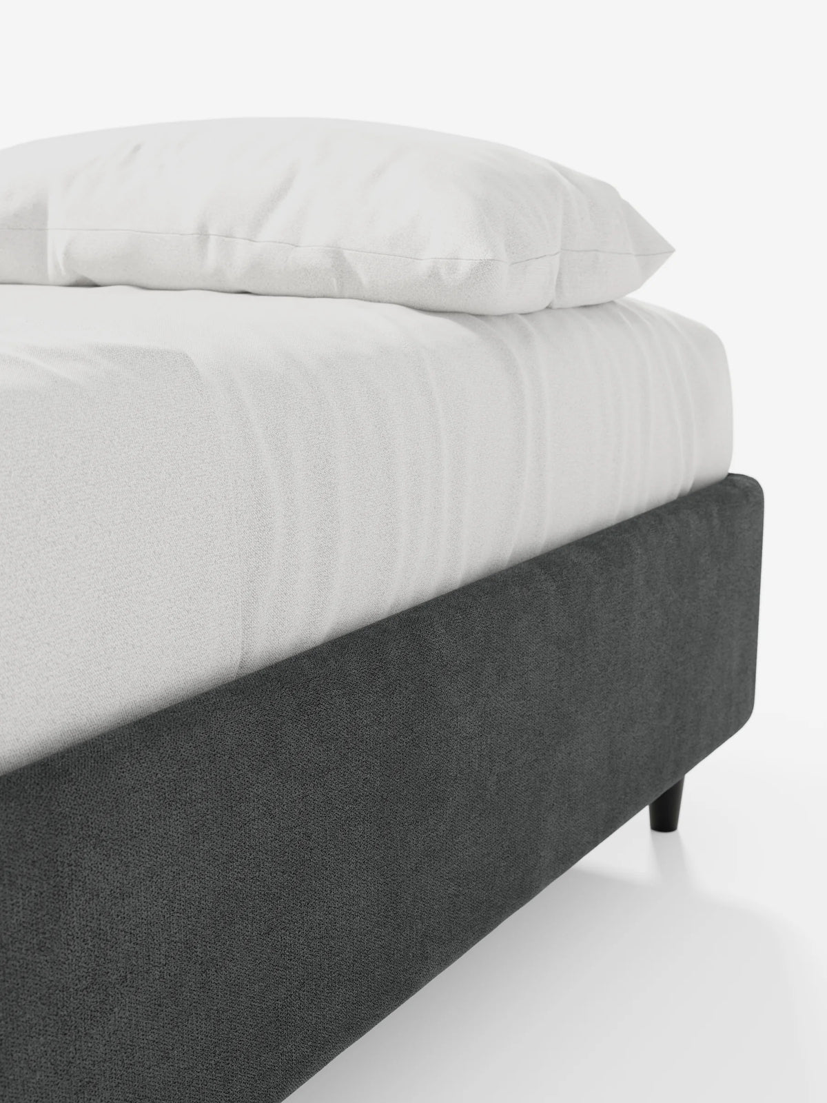 Il letto sommier imbottito ERON con vano contenitore in tessuto impermeabile certificato Oeko-Tex è una struttura da letto bassa, di colore grigio antracite, con gambe corte nere, raffigurata con un materasso e un cuscino di un bianco brillante su uno sfondo bianco a tinta unita.