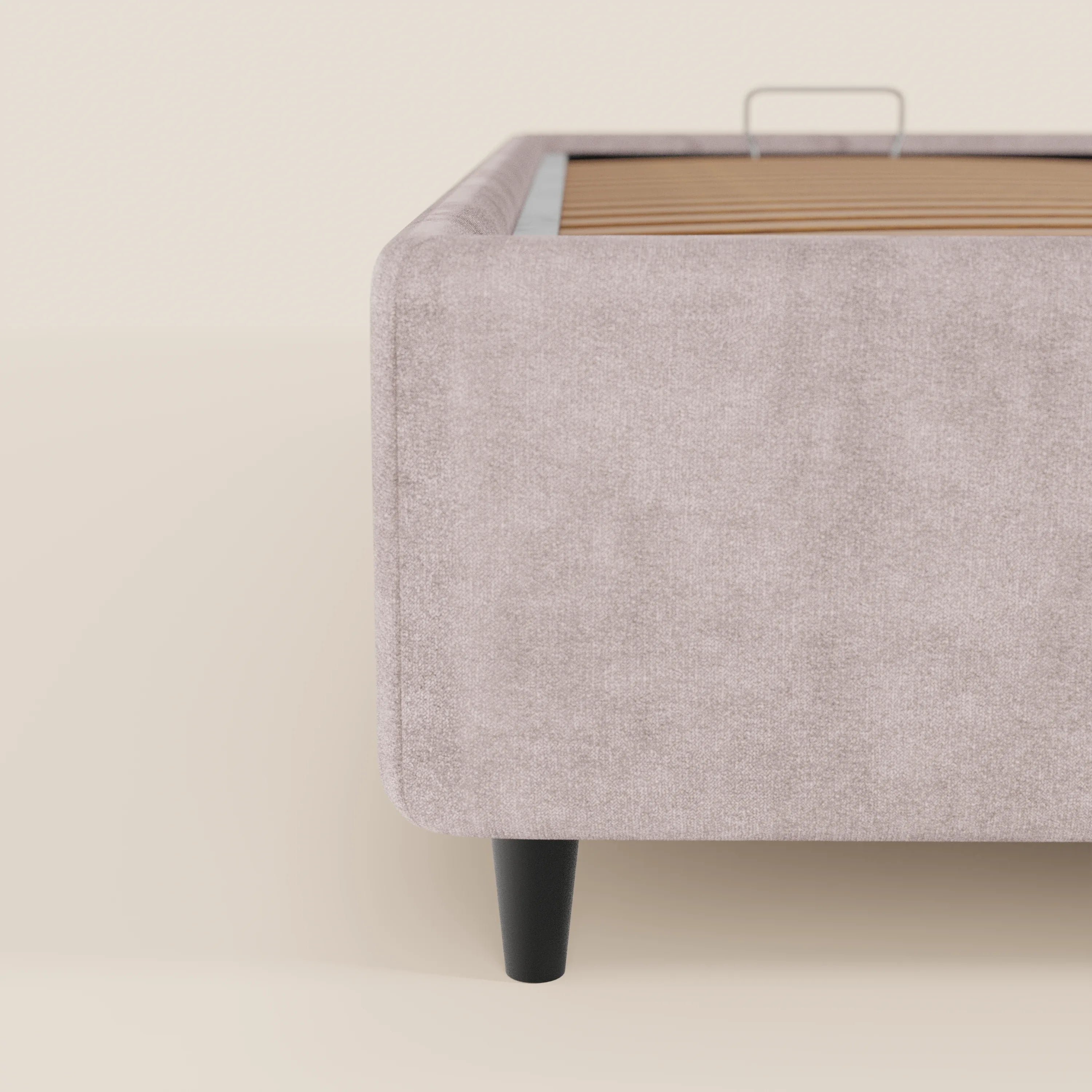 Primo piano della vista laterale del letto sommier imbottito ERON di Letti.store, caratterizzato da un tessuto beige chiaro impermeabile certificato Oeko-Tex, doghe in legno, un’unica gamba nera affusolata e un ampio vano contenitore. L’estetica minimalista risalta sullo sfondo coordinato.