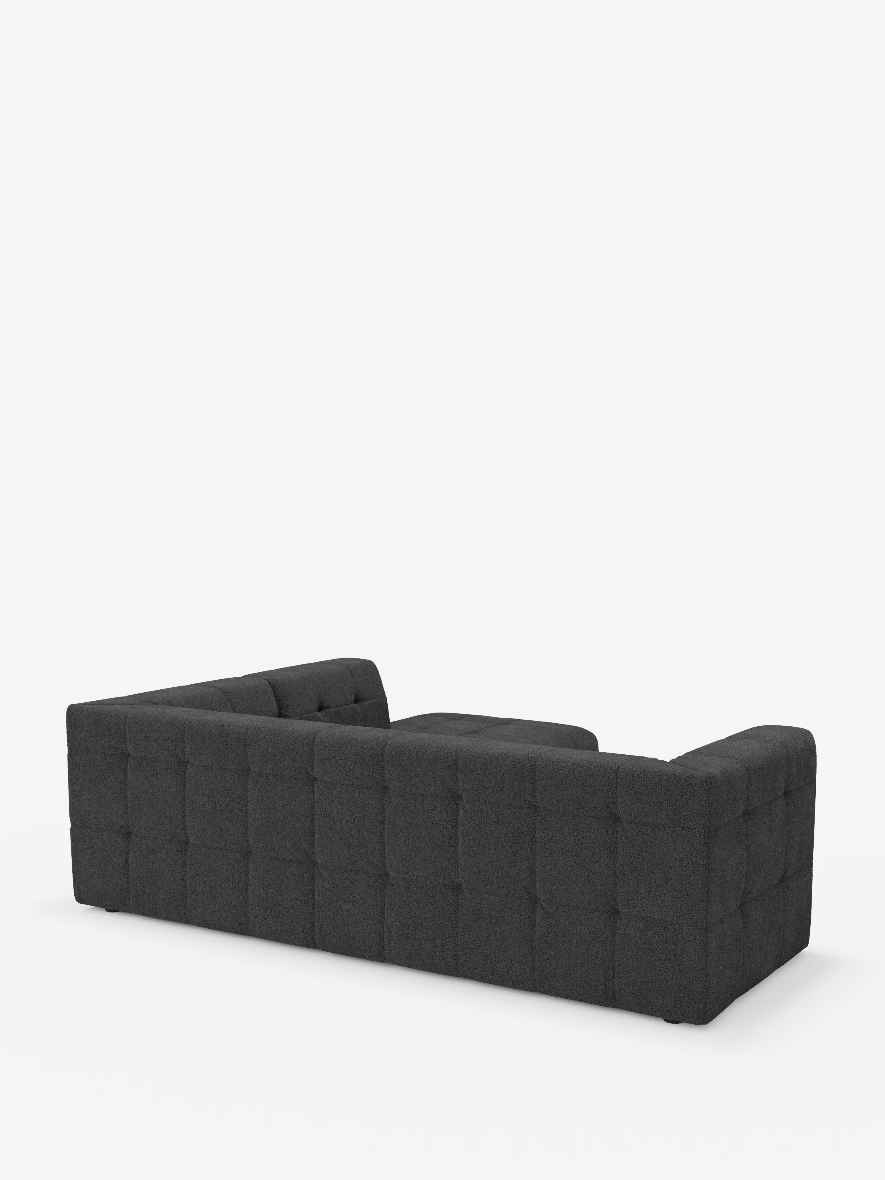 Un divano angolare componibile e modulare Mosaic, moderno e di colore grigio scuro, realizzato in bouclé da Divani.Store, caratterizzato da un motivo quadrato capitonné sui fianchi e sullo schienale, è raffigurato su uno sfondo bianco e ripreso da dietro in un’angolazione obliqua. Il rivestimento in tessuto T21, morbido e resistente alle macchie, e le linee pulite e contemporanee lo rendono ideale per un soggiorno moderno.