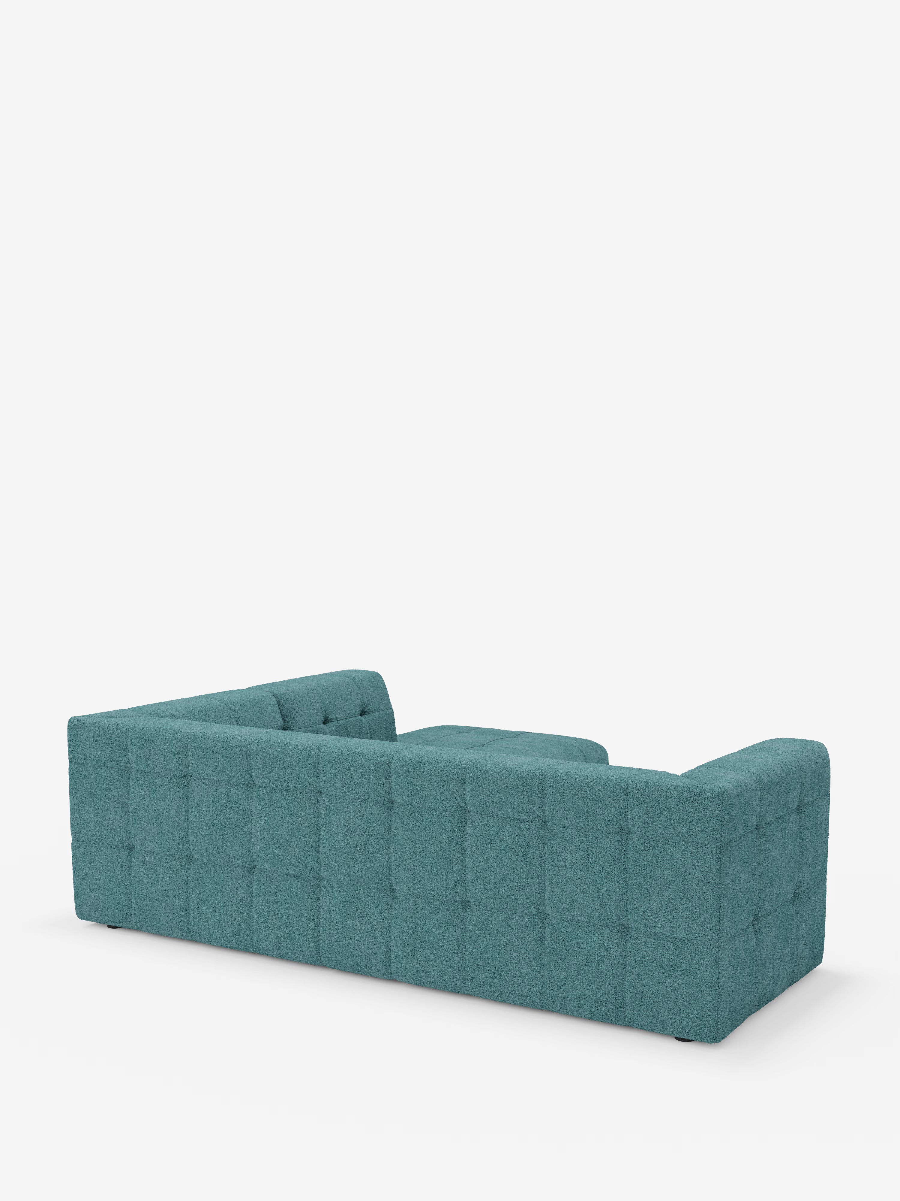 Un moderno divano angolare componibile e modulare Mosaic in blu verde acqua, realizzato in bouclé da Divani.Store, caratterizzato da schienale e braccioli bassi, rivestito in tessuto T21 capitonné con motivo a griglia e resistente alle macchie. Questo elegante divano componibile è ripreso da dietro e leggermente di profilo, su uno sfondo bianco a tinta unita.