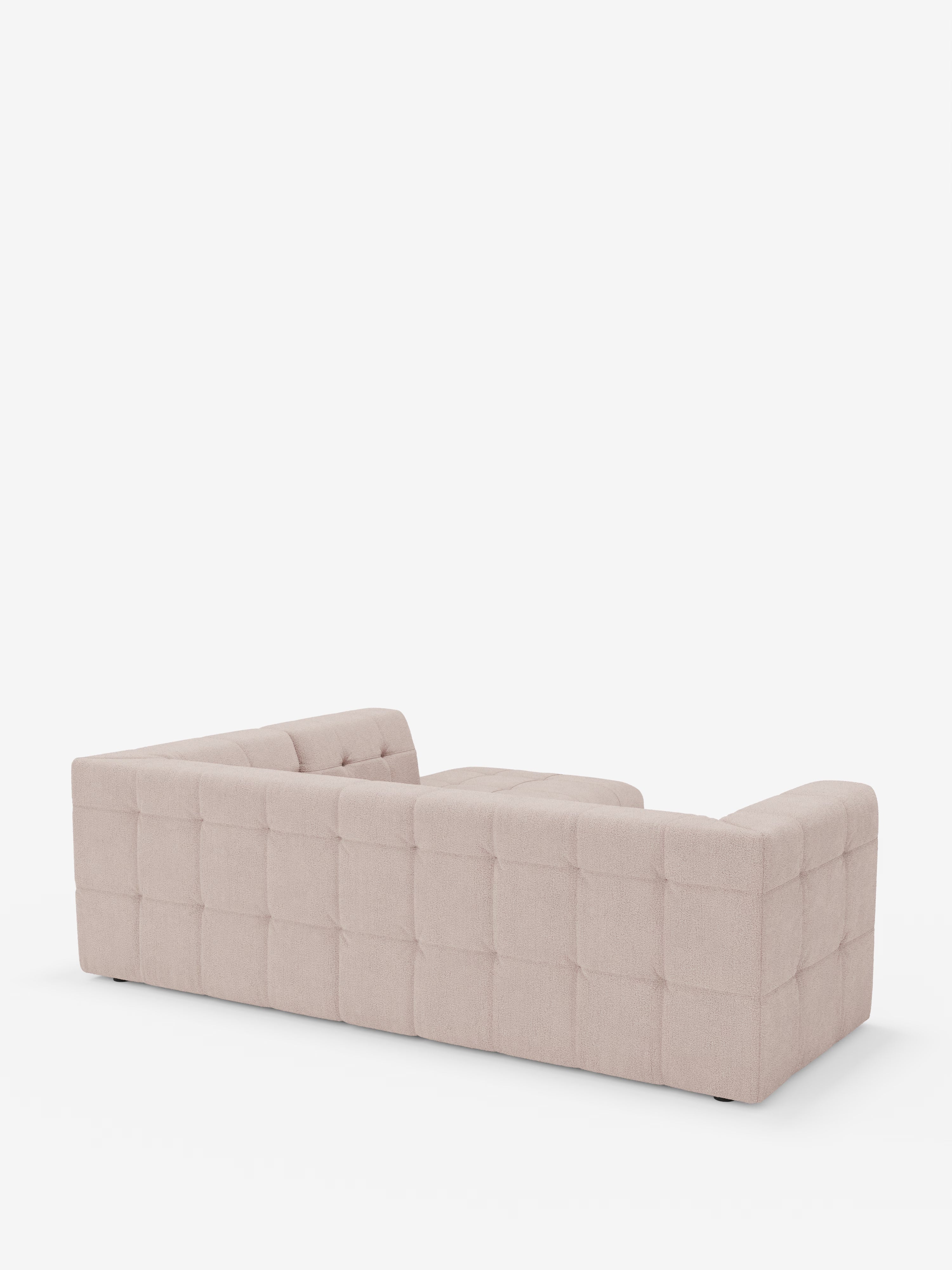 Un divano angolare componibile e modulare “Mosaic” di Divani.Store, in bouclé beige, è ripreso da dietro in un'inquadratura obliqua. La sua silhouette squadrata e il rivestimento capitonné a griglia, realizzato in tessuto T21 resistente alle macchie, risaltano su uno sfondo bianco, senza altri oggetti visibili.