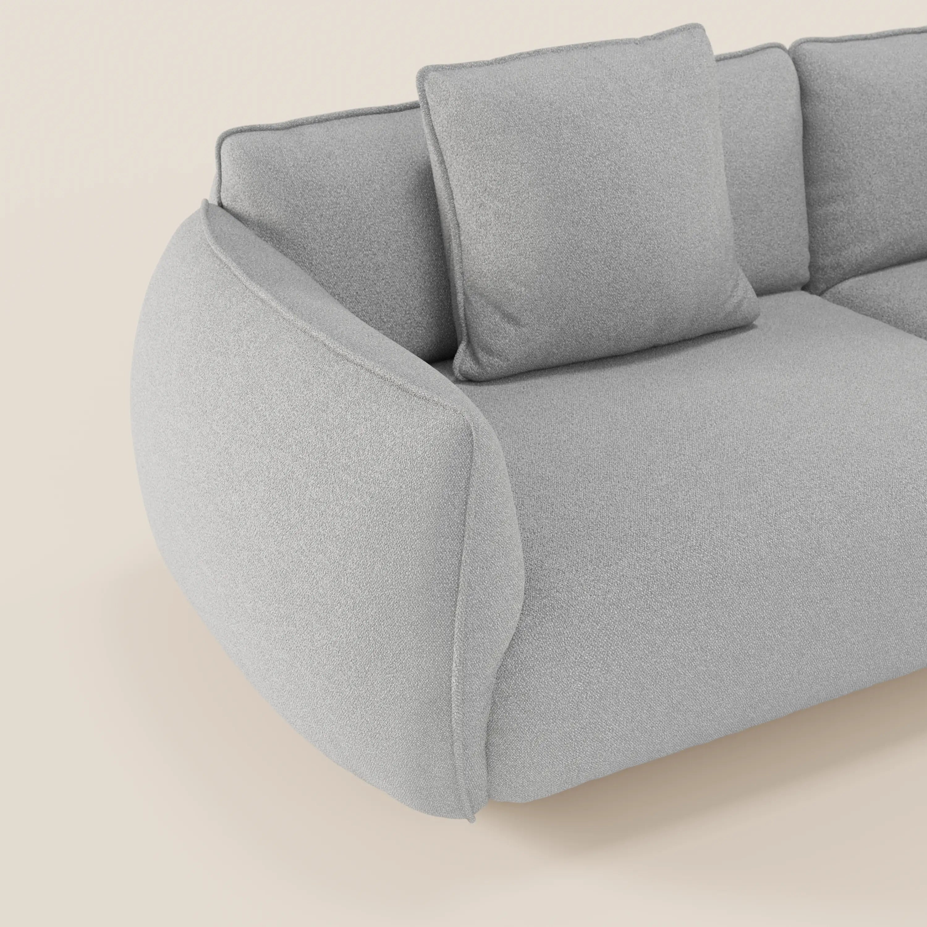 Primo piano del divano Nimbus 3 posti modulare e componibile 250 cm di Divani.Store, in smacchiabile tessuto effetto cotone t33 grigio chiaro, con bordi arrotondati e cuscino quadrato, su sfondo panna. Stile accogliente e contemporaneo.