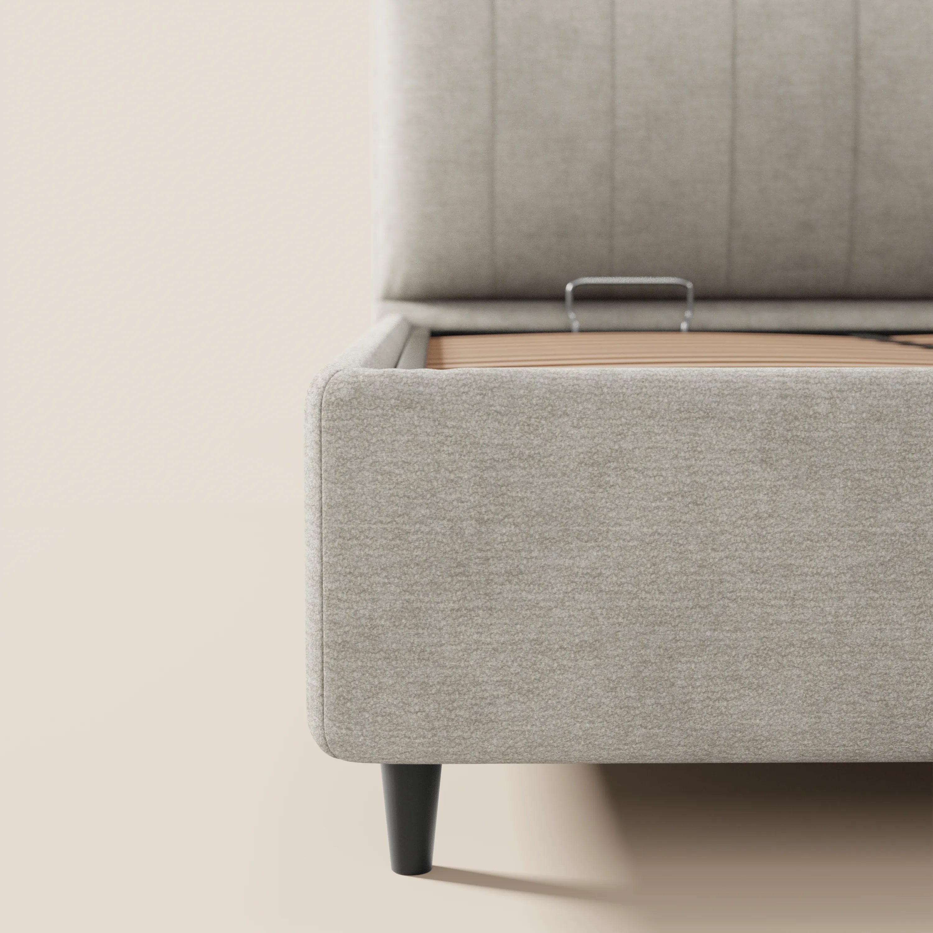 Primo piano del letto imbottito ONYX di Letti.store, realizzato in tessuto grigio chiaro certificato Oeko-Tex®, che mostra il vano contenitore con maniglia in metallo, la testiera alta verticale con cuciture verticali e le gambe corte nere su uno sfondo neutro.