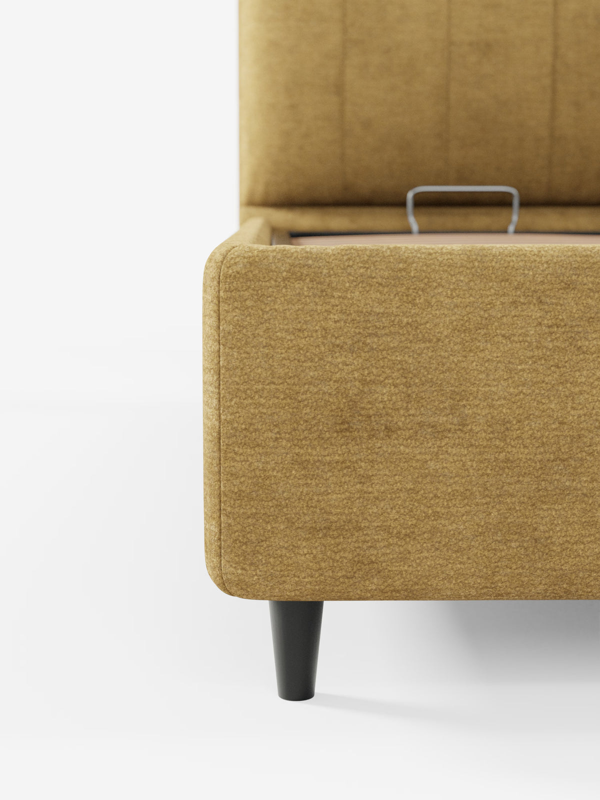 Primo piano dell'angolo di un letto imbottito ONYX con vano contenitore e testiera verticale di Letti.store, qui raffigurato in giallo senape con gambe corte, nere e angolate. Il coperchio del vano contenitore è parzialmente aperto, lasciando intravedere un'elegante maniglia in metallo. Su uno sfondo bianco a tinta unita, il tessuto certificato Oeko-Tex® e la raffinata lavorazione artigianale mettono in risalto il fascino moderno e l’attenzione ai dettagli che contraddistinguono questo letto moderno dal