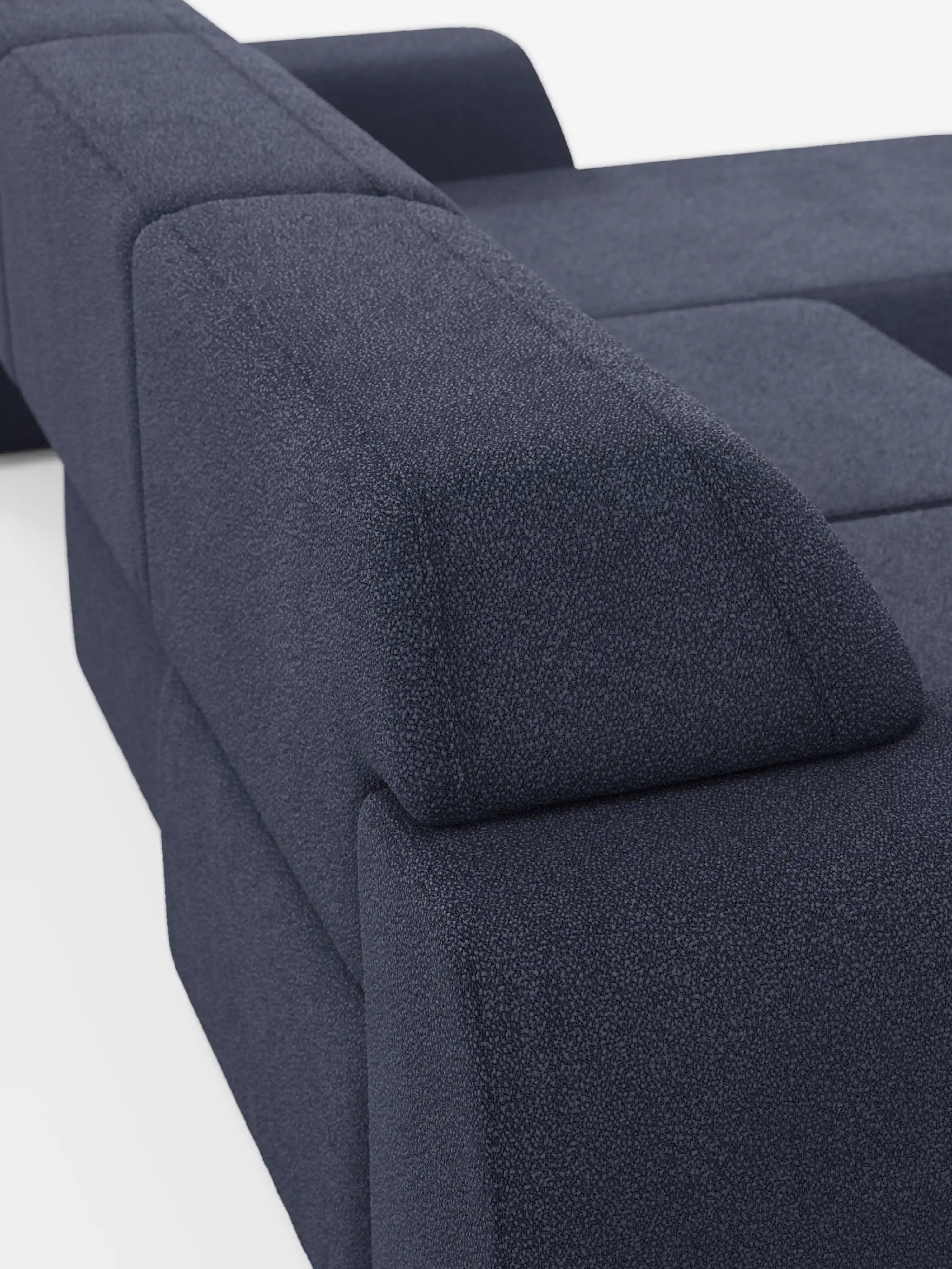 Primo piano del divano angolare Orbit con penisola reversibile e tutte le sedute allungabili in tessuto smacchiabile effetto cotone T33 di Divani.Store, caratterizzato da un rivestimento blu intenso con effetto testurizzato, linee geometriche pulite, braccioli squadrati e cuscini dal profilo massiccio. Presentato su uno sfondo bianco, questo design minimalista e modulare esalta il comfort contemporaneo: un vero divano di alta gamma, ideale per interni sofisticati.